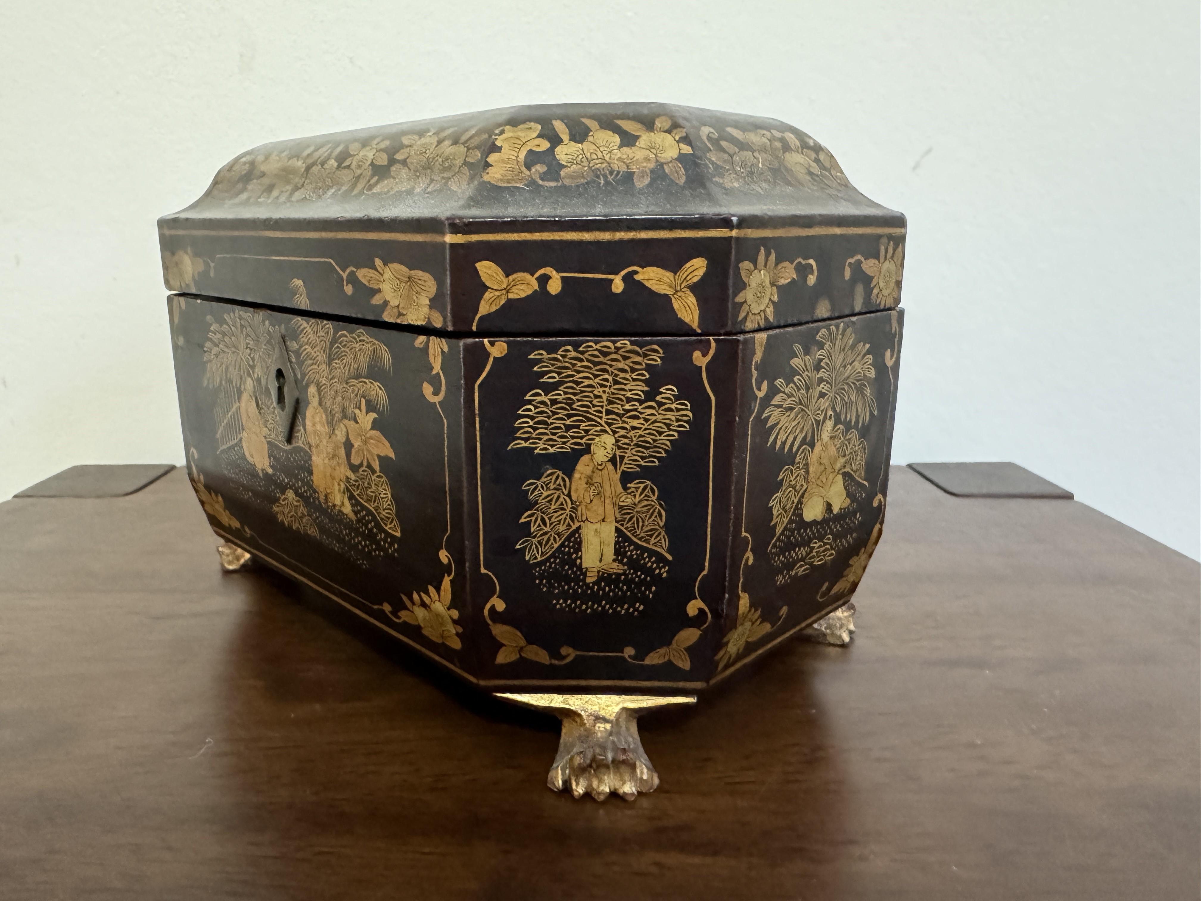 A 19th Century Lacquered Papier Mache Tea Caddy of rectangular form with an ogee moulded edge and canted corners decorated with chinoiserie figures and bands of flowers. Standing on gilded lion paw feet 8 ins x 5 ins x 5 ins (20 cm x 13 cm x 13 cm).