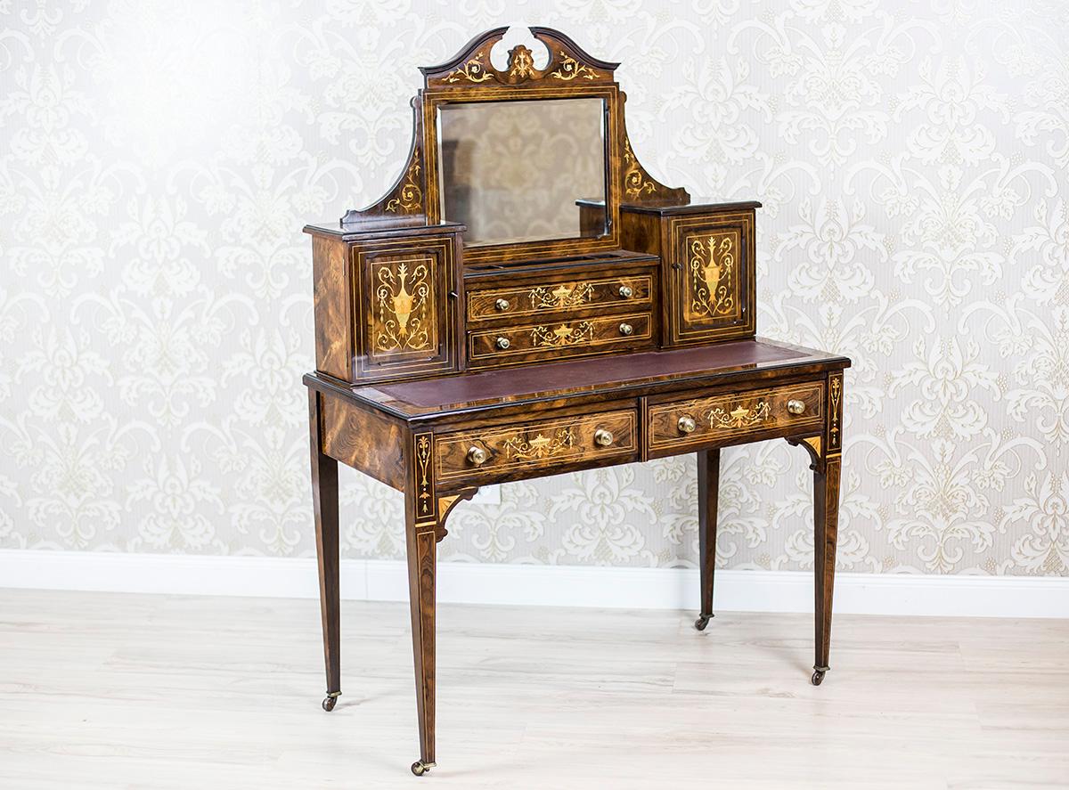 We present you a lady’s desk covered with rosewood veneer, dated 1880.
This piece of furniture is of a rectangular form of a small table with two drawers; placed on thin, high legs.
Moreover, it has an add-on unit with a mirror, cabinets, and