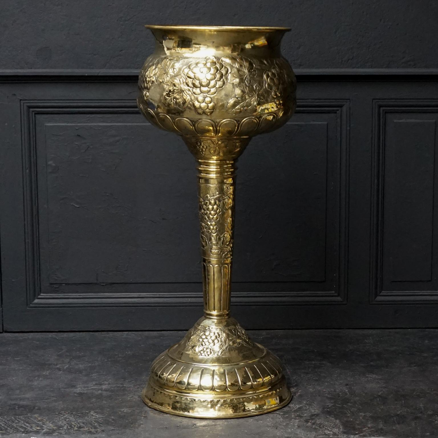 A very large, oversized hand-hammered brass cachepot or on a high leg, also usable as Champagne ice bucket
The leg and the bulbous repoussé body are decorated with hammered bunches of grapes, grape leaves and stylish decorations. 
In the middle of