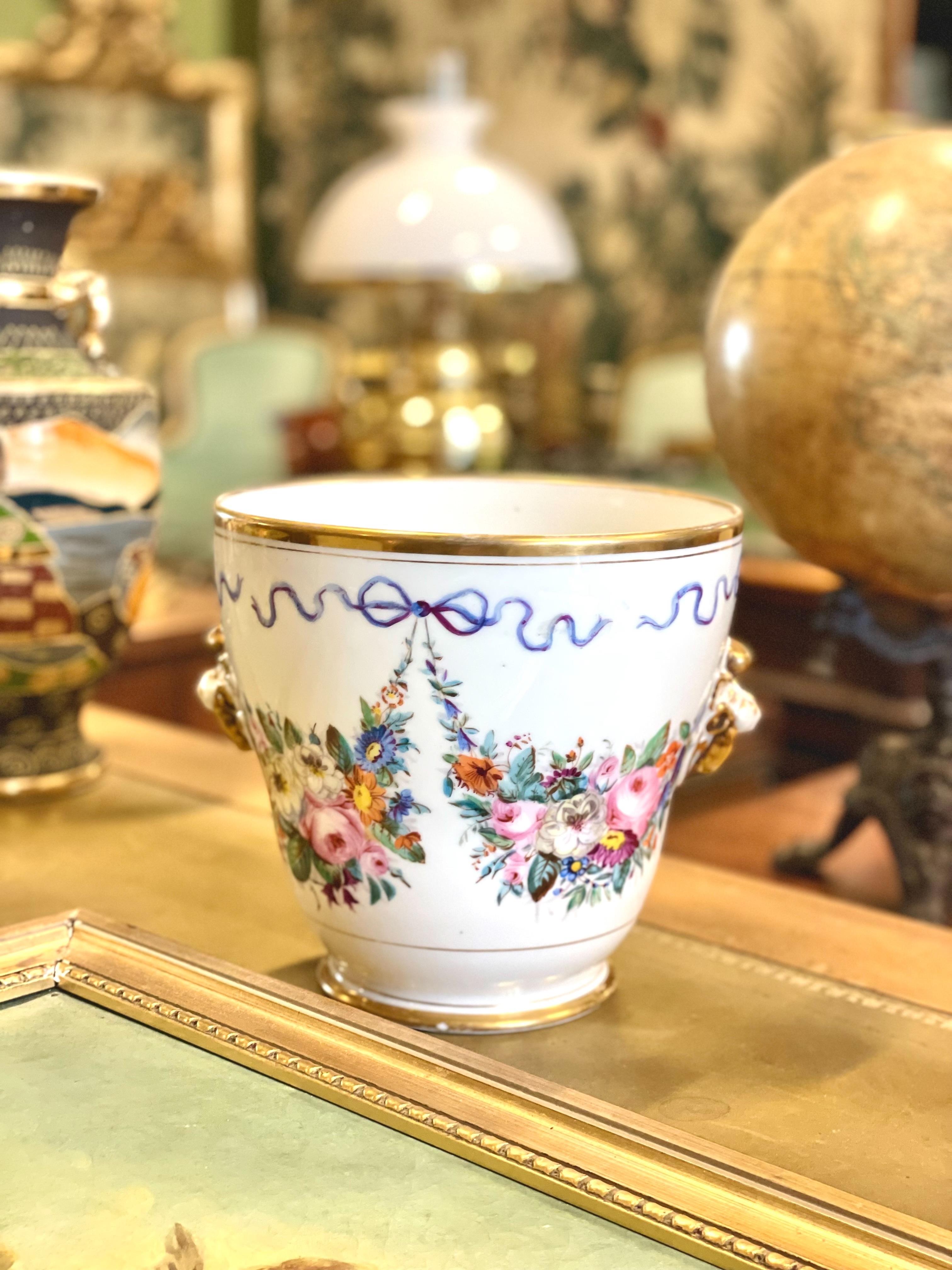 Questo cachepot francese, risalente agli inizi del XIX secolo, è un raffinato esempio dello stile Luigi XVI, caratterizzato da eleganza e simmetria classica. Il pezzo di porcellana è ornato da intricati motivi floreali dipinti a mano con vivaci