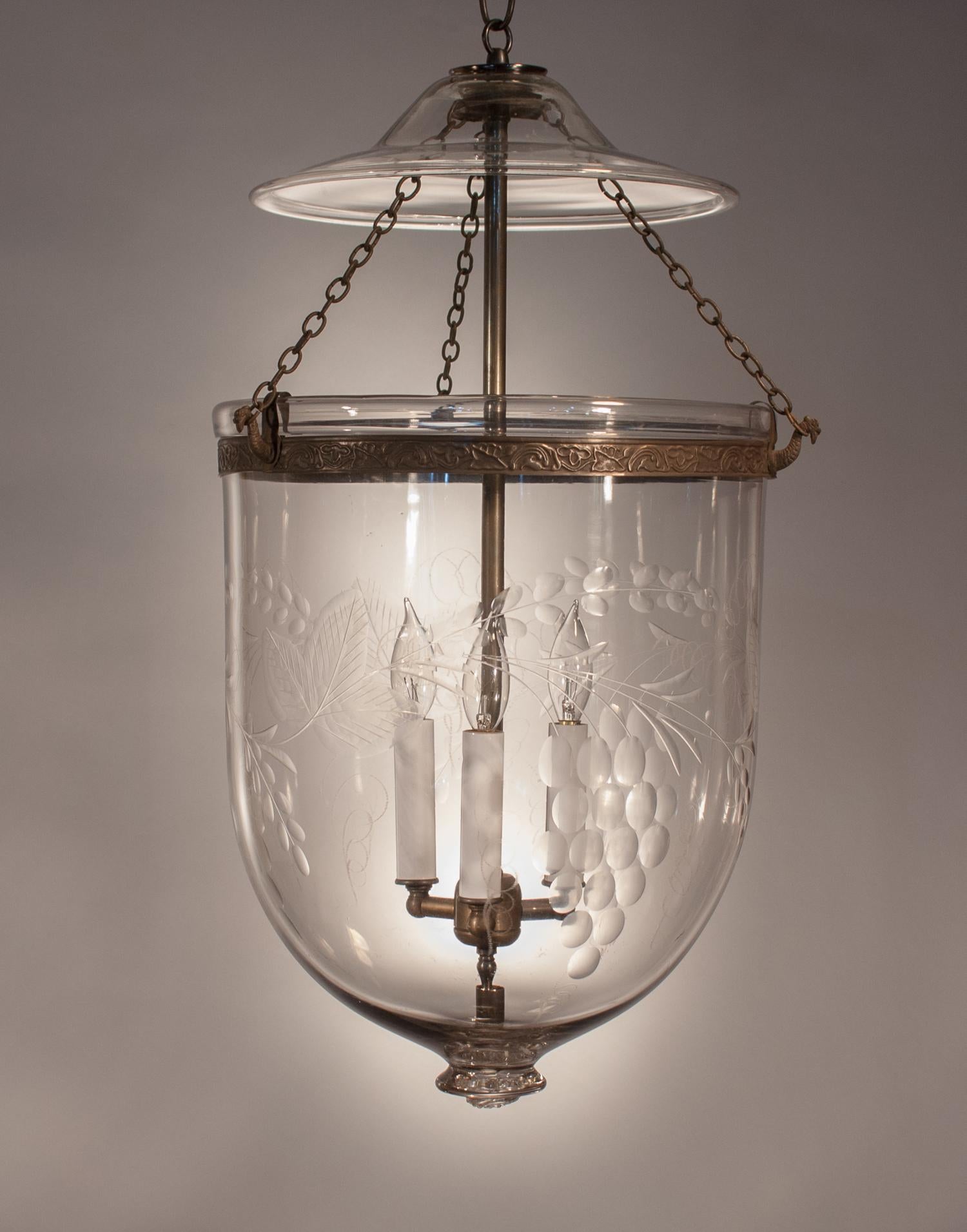 A substantial English handblown glass bell jar lantern with lovely form and an attractive grape with leaf polished etching. The hall lantern has its original smoke bell. Its chains and brass band, which has an embossed vine design, have been