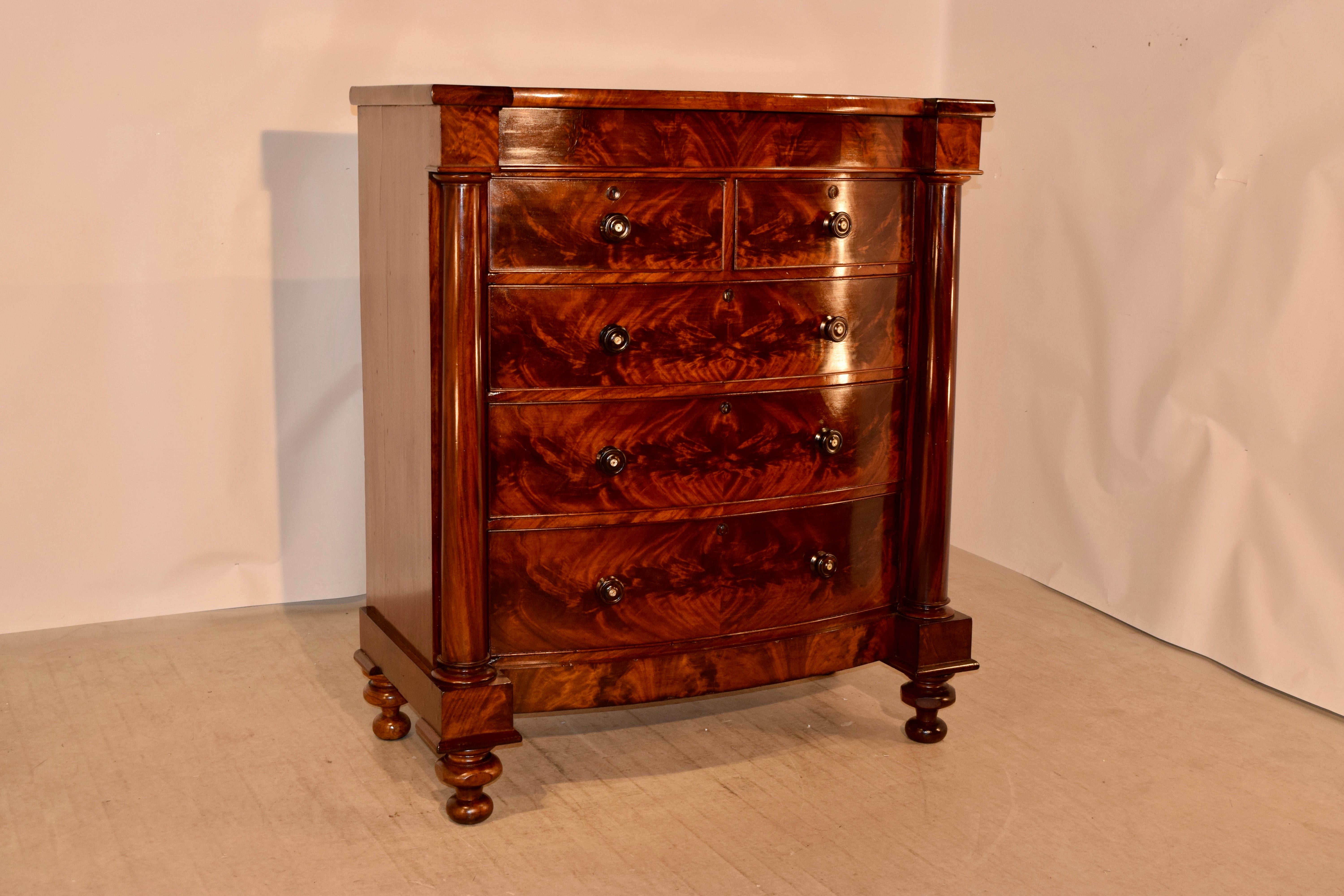 19th century large mahogany bowfront chest of drawers from England with a shaped top, following down to beautifully grained sides and a hidden drawer at the top over two smaller drawers and three larger drawers, which are flanked by blocked columns.