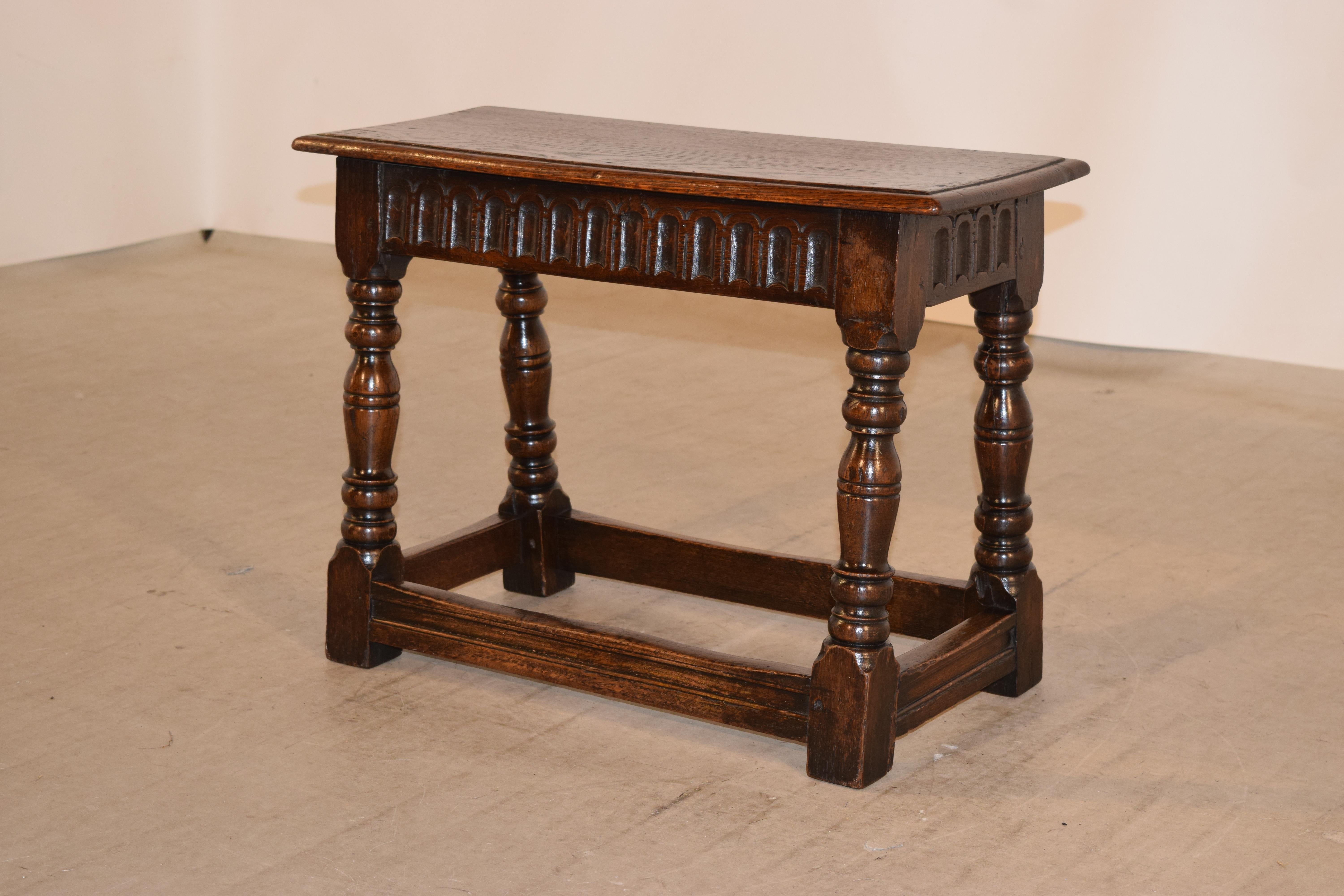 19th century large English oak stool with a beveled edge around the pegged top, following down to a hand carved decorated fluted apron and supported on splayed hand-turned legs, joined by routed stretchers. Seat depth is 10.25 inches.