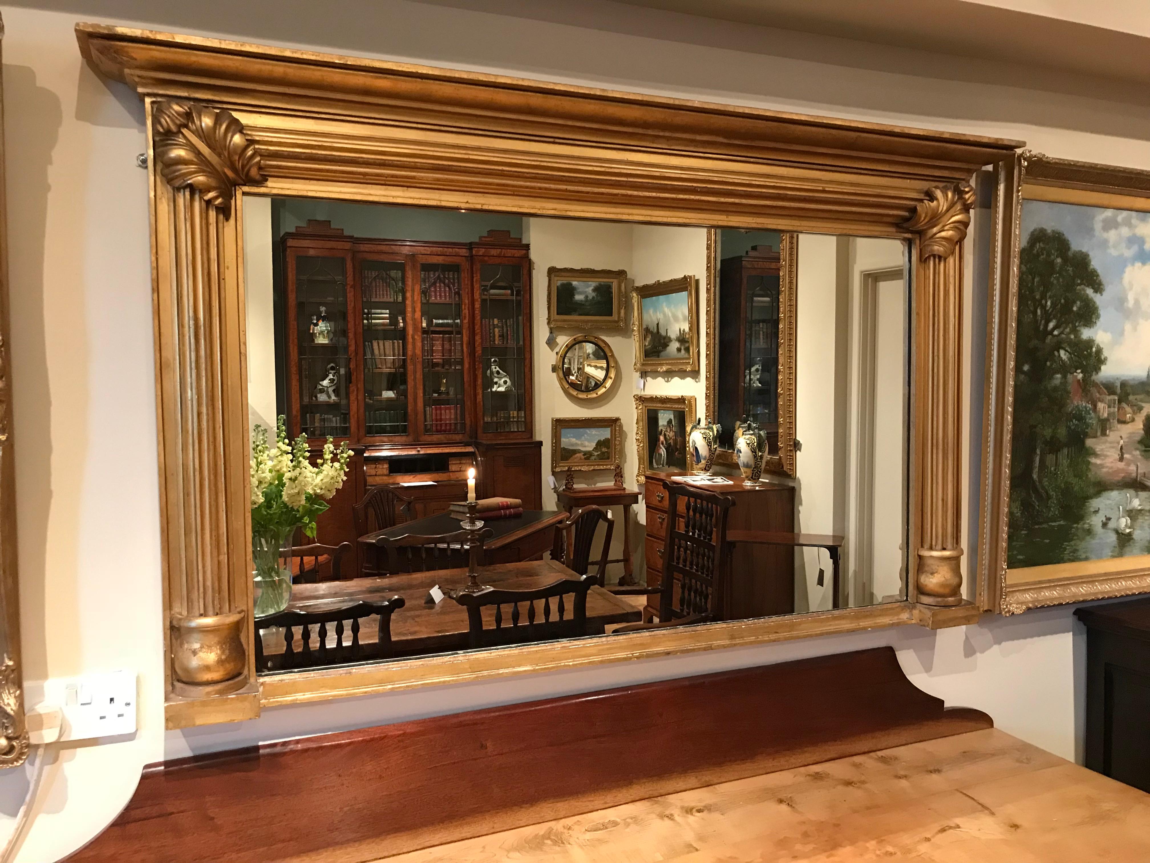 19th century large giltwood rectangular overmantel mirror, with a projecting moulded cornice, the inset mirror plate flanked by fluted half columns with applied acanthus leaf decoration.