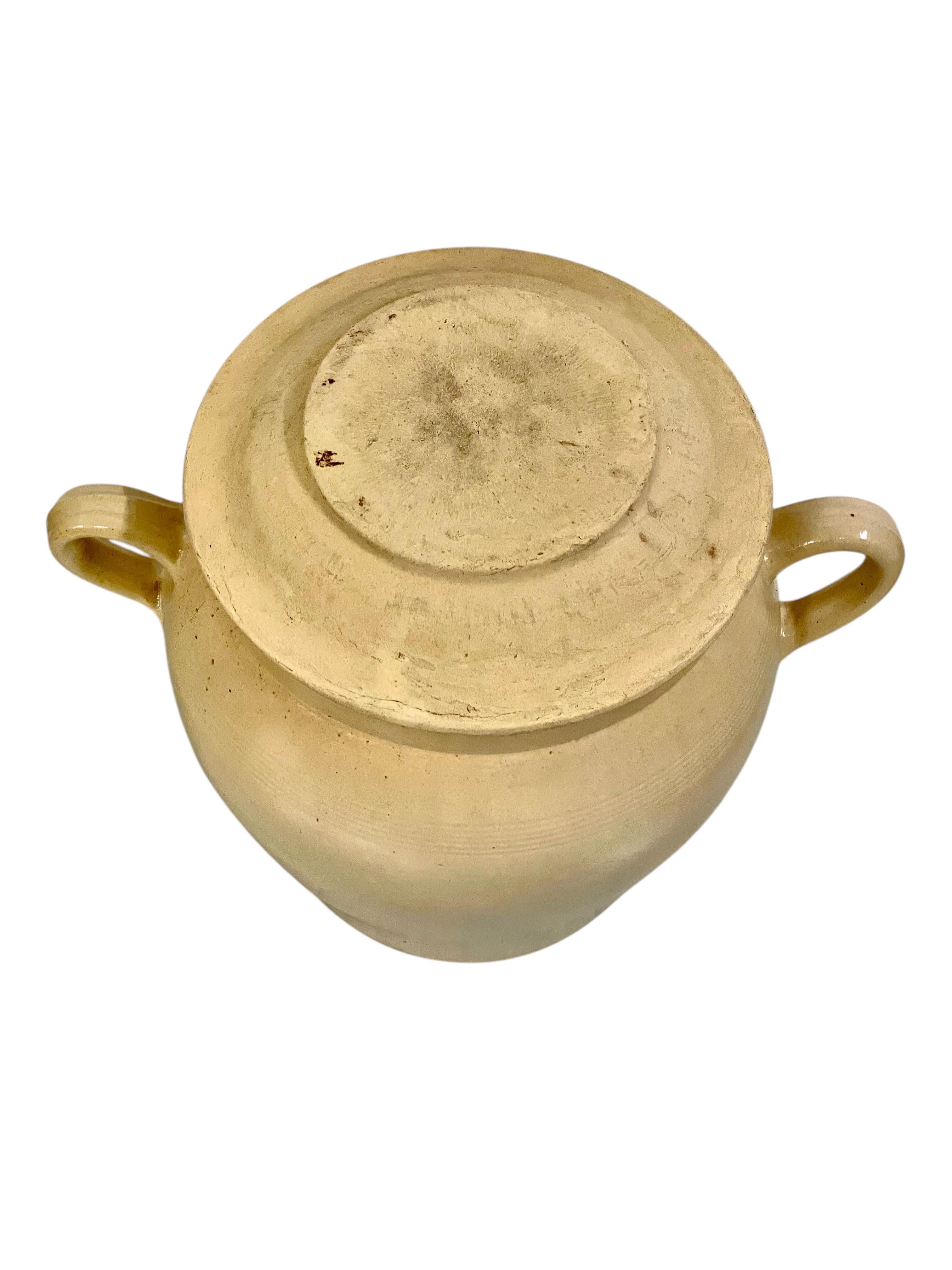 Ce grand pot en grès français magnifiquement préservé date du XIXe siècle et incarne l'élégance rustique de la poterie rurale française traditionnelle. Fabriqué en terre cuite durable et recouvert d'une douce glaçure beige, ce récipient aux