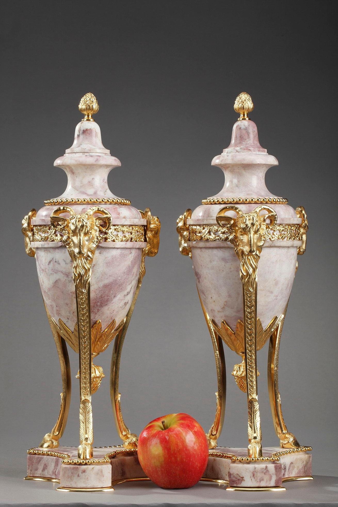 A large pair of Louis XVI-style covered urns, or cassolettes, crafted of pink-white marble and gilt bronze mounts. The cassolette vases are finely chiseled with interlacing and intricate foliate accents, including an olive branch. The feet are