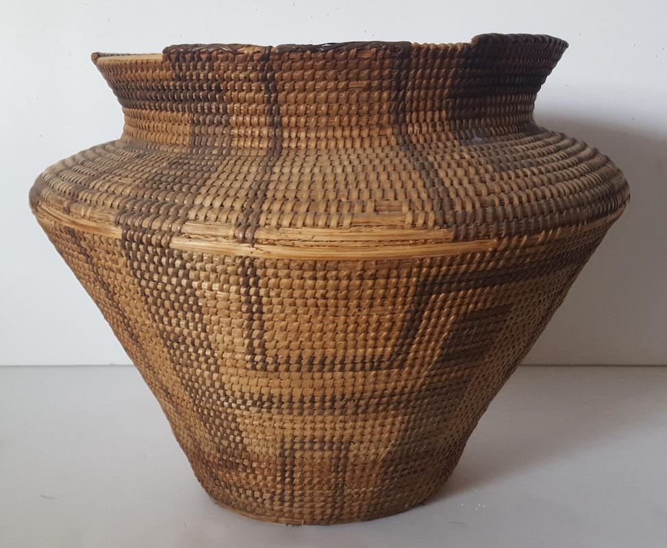This large, hand woven basket, likely Pima-Papago, or similar Southwestern Native American Tribe, is in worn condition from much use, and has lost it's symmetrical shape. It lists or leans a bit to one side and has several losses of woven grasses on