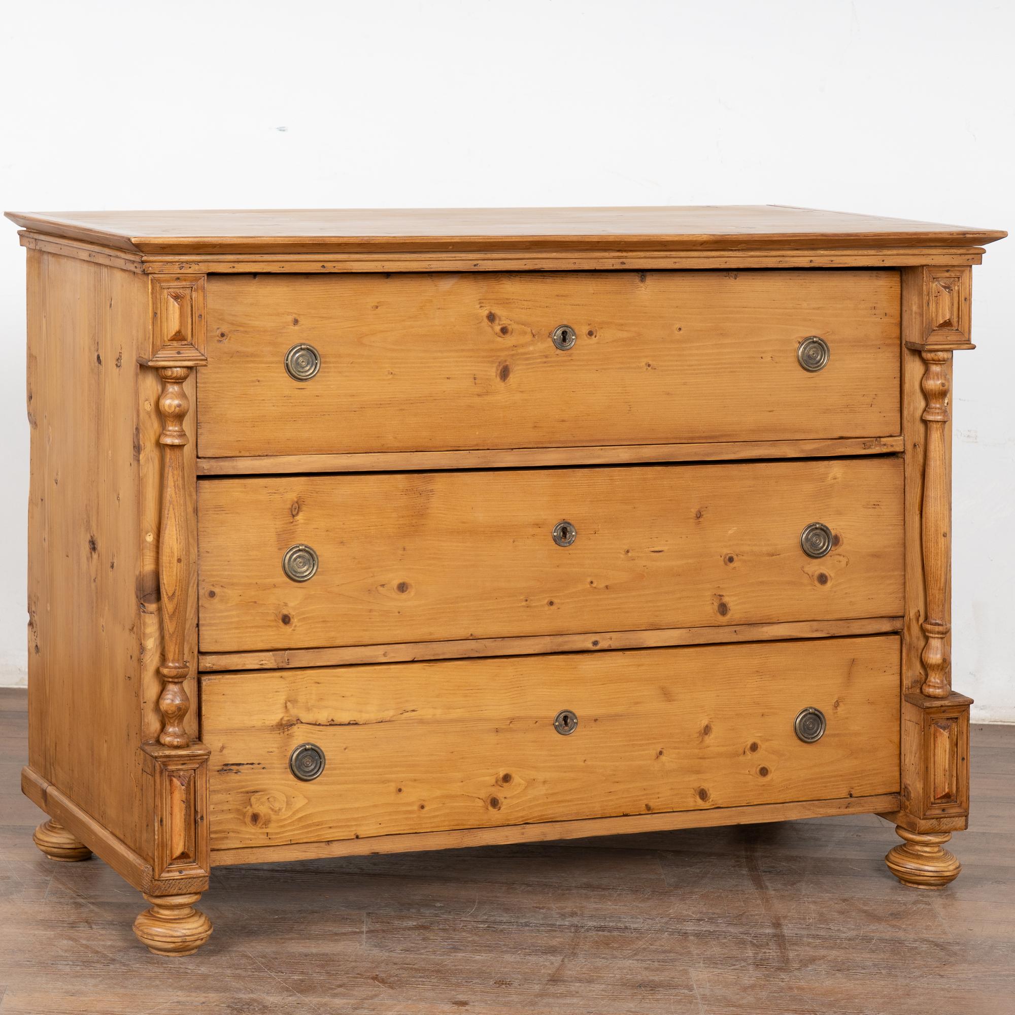 Antique large pine chest of three drawers resting on bun feet.
Traditional turned column details, dove-tail joints and brass pulls.
Note the natural wax finish that brings out the warmth of the pine. 
Restored, this large dresser or blanket chest is