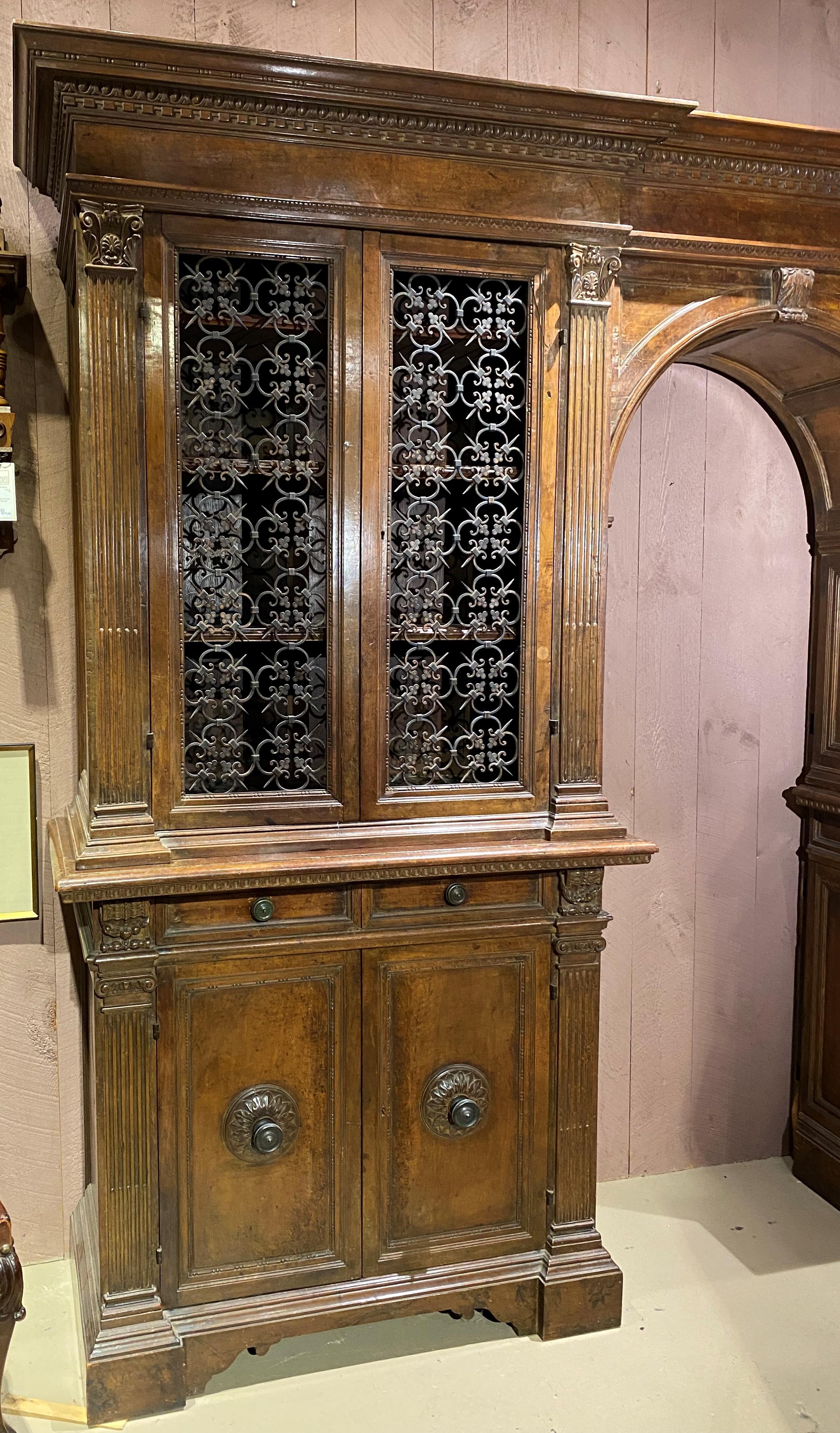 An exceptional Renaissance style large walnut cabinet with nicely carved cornice surmounting a center arch flanked by upper single cabinet doors featuring open decorative wrought iron metalwork fronts, opening to three removable shelves on the left