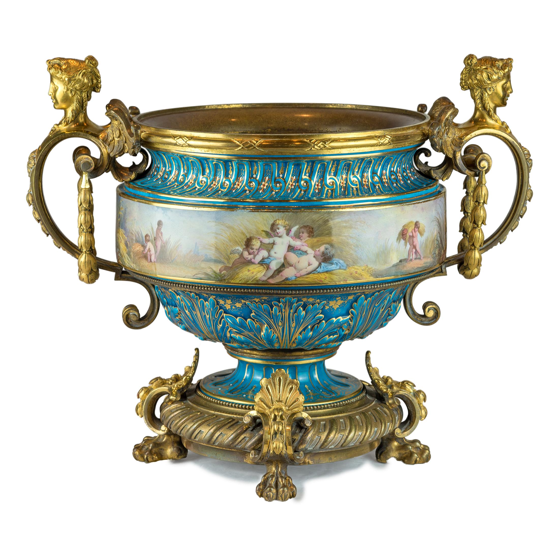 A fine quality large sevres-style and gilt bronze centerpiece.
Hand painted porcelain with frolicking putti in landscape. Surrounded by heavy bronze mounts with winged female caryatid handles raised on claw feet. 

Origin: French
Date: 19th