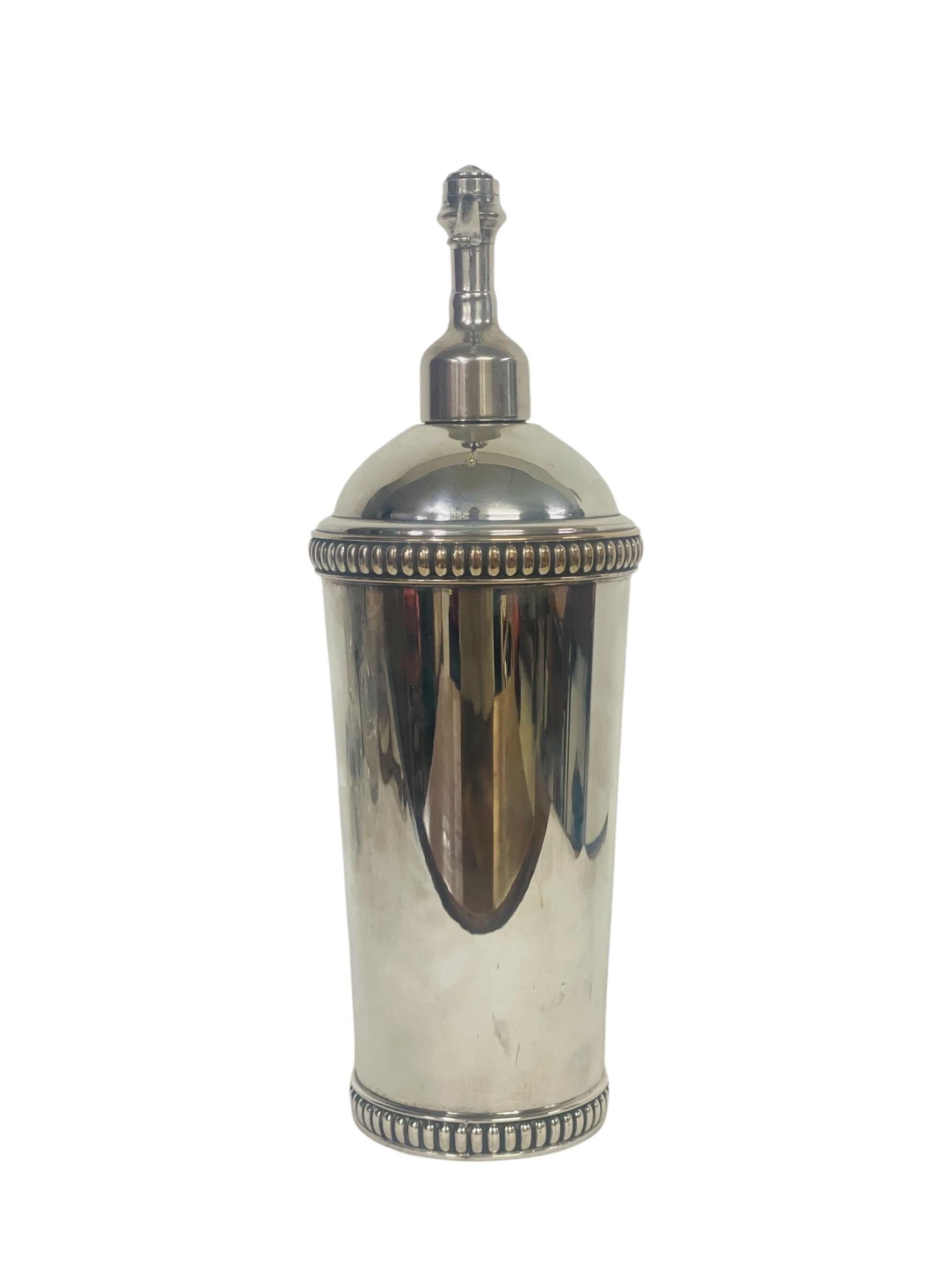 
This antique silver-plated seltzer syphon is a stunning example of 19th-century craftsmanship. Its elegant cylindrical form is adorned with intricate beaded detailing at both the top and bottom, adding a touch of opulence. The syphon's smooth,