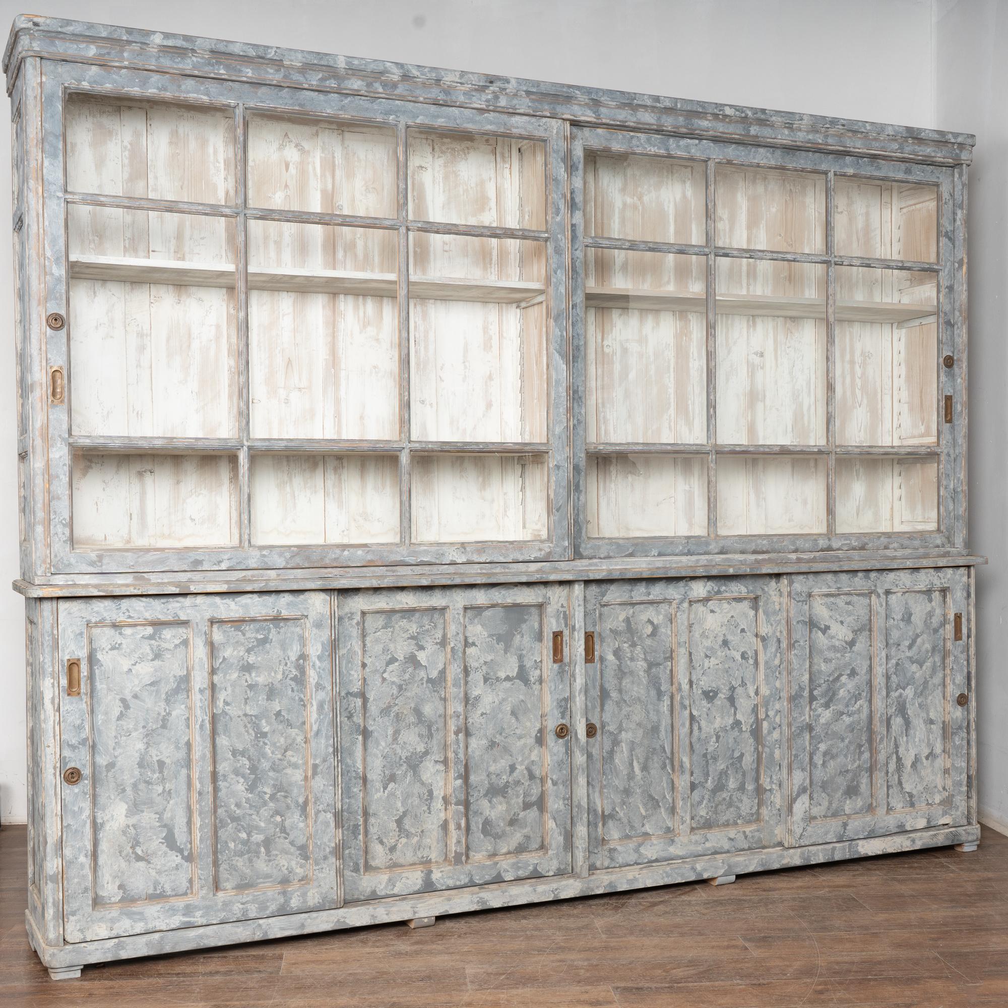 Swedish country 10' long pine display cabinet or bookcase in two sections. Two large sliding upper glass doors over four paneled sliding lower cabinet doors.
Pine wood newer professionally painted in blue and white with a blue/gray appearance,