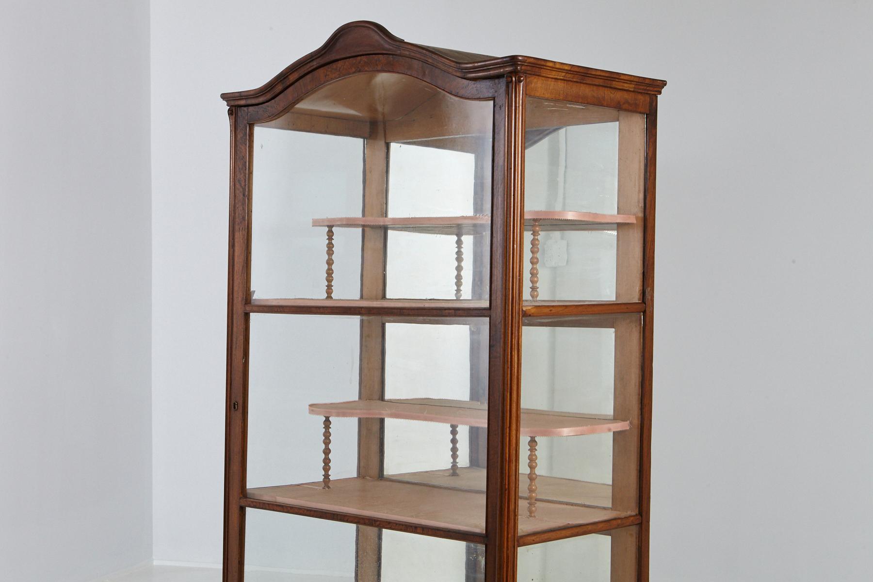 A lovely and light walnut cabinet/vitrine, with one original large glass door, glass side panels, and a mirrored back. Two large shelves with two recessed half shelves covered in fabric and a hand carved bonnet.
The key is present, just not on the