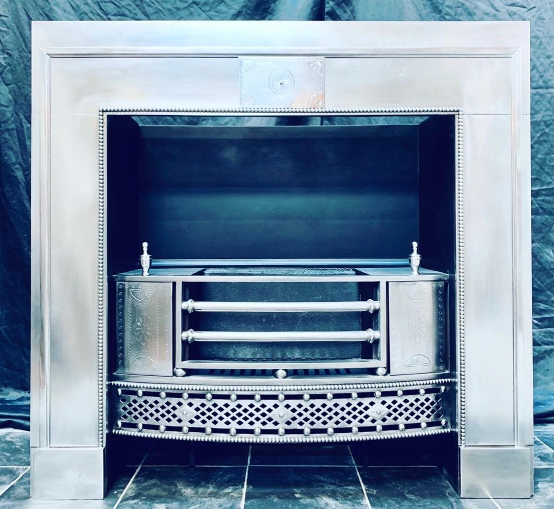 A very elegant polished steel late Georgian register fireplace insert grate, a central etched tablet within a repeating beaded border and framed with an outer raised bar moulding. A bowed three barred grate resting on cushion spacers, flanked by
