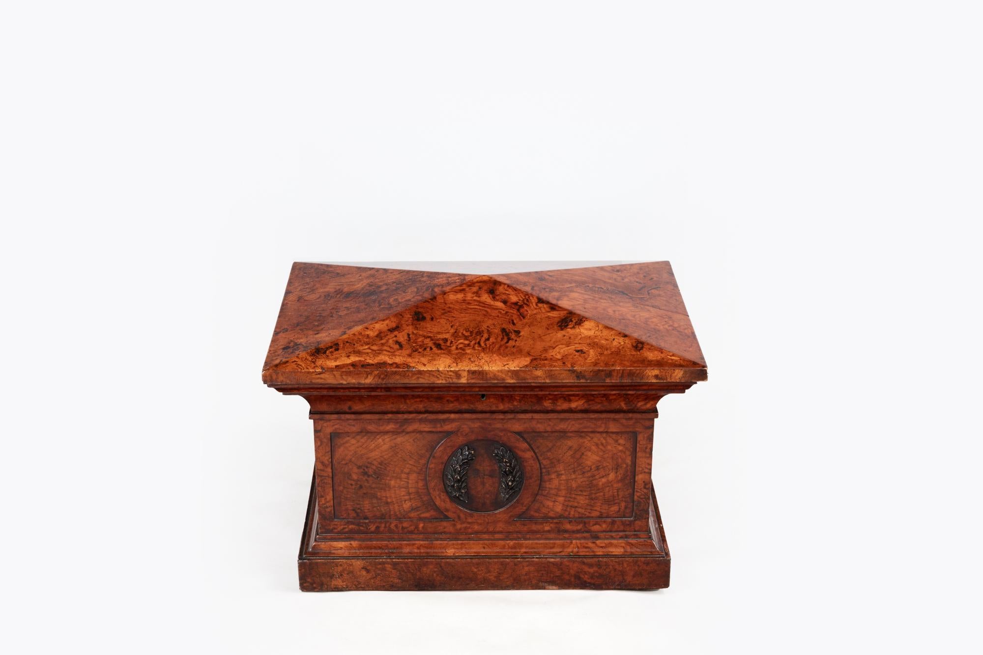 19th Century late Regency pollard oak sarcophagus form cellarette stamped Wilkinsons & Sons, 14 Ludgate Hill, the hinged lid enclosing a six division lined interior with brass ratchet support. The front features a carved laurel wreath motif within a