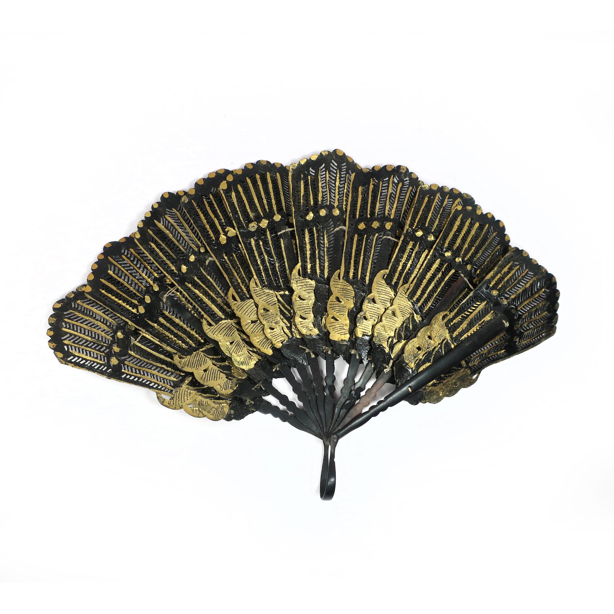 A stunning and rare example of a 19th century hand fan, made of black leather and decorated with gold leaf. The fan has a brisé style, meaning that it consists of narrow sticks that are connected at the top and can be folded together. The sticks are