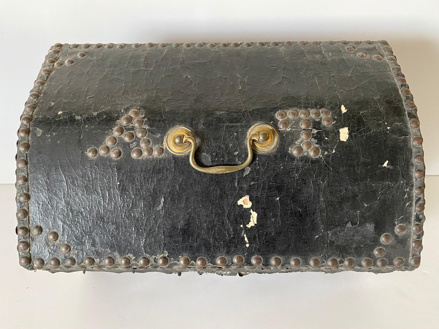 This small box for personal possessions (perhaps papers or letters), is covered in black leather and decorated with borders of brass tacks, including the letters A.T. on its lid, and two diamond shapes and a heart shape on the front side face. The