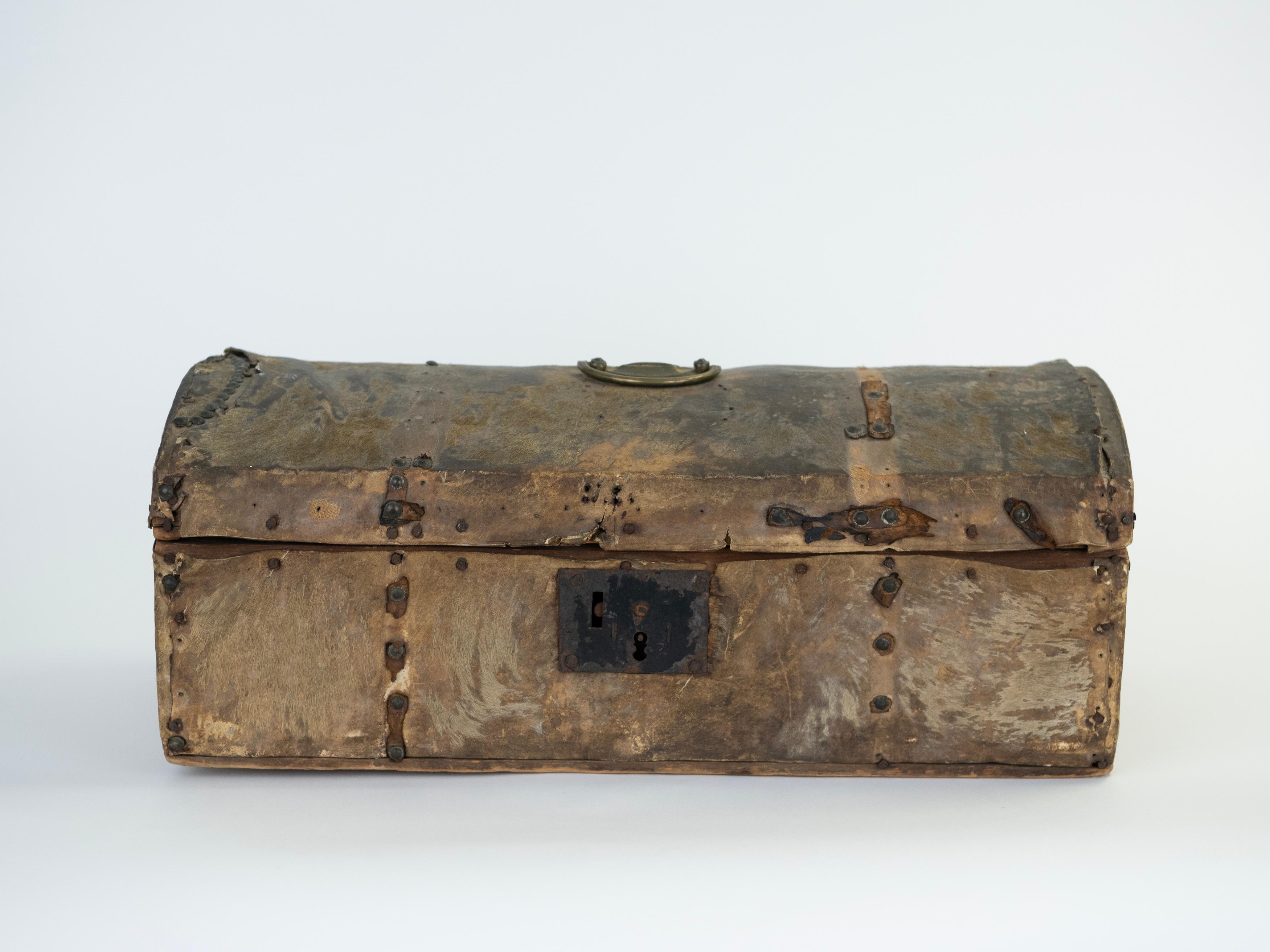 An evocative 19th-century Argentine travel chest, constructed with a wood carcass tightly wrapped in natural cowhide and reinforced with hand- forged iron strapping. The domed lid-designed to shed dust and moisture during overlap travel-retains its