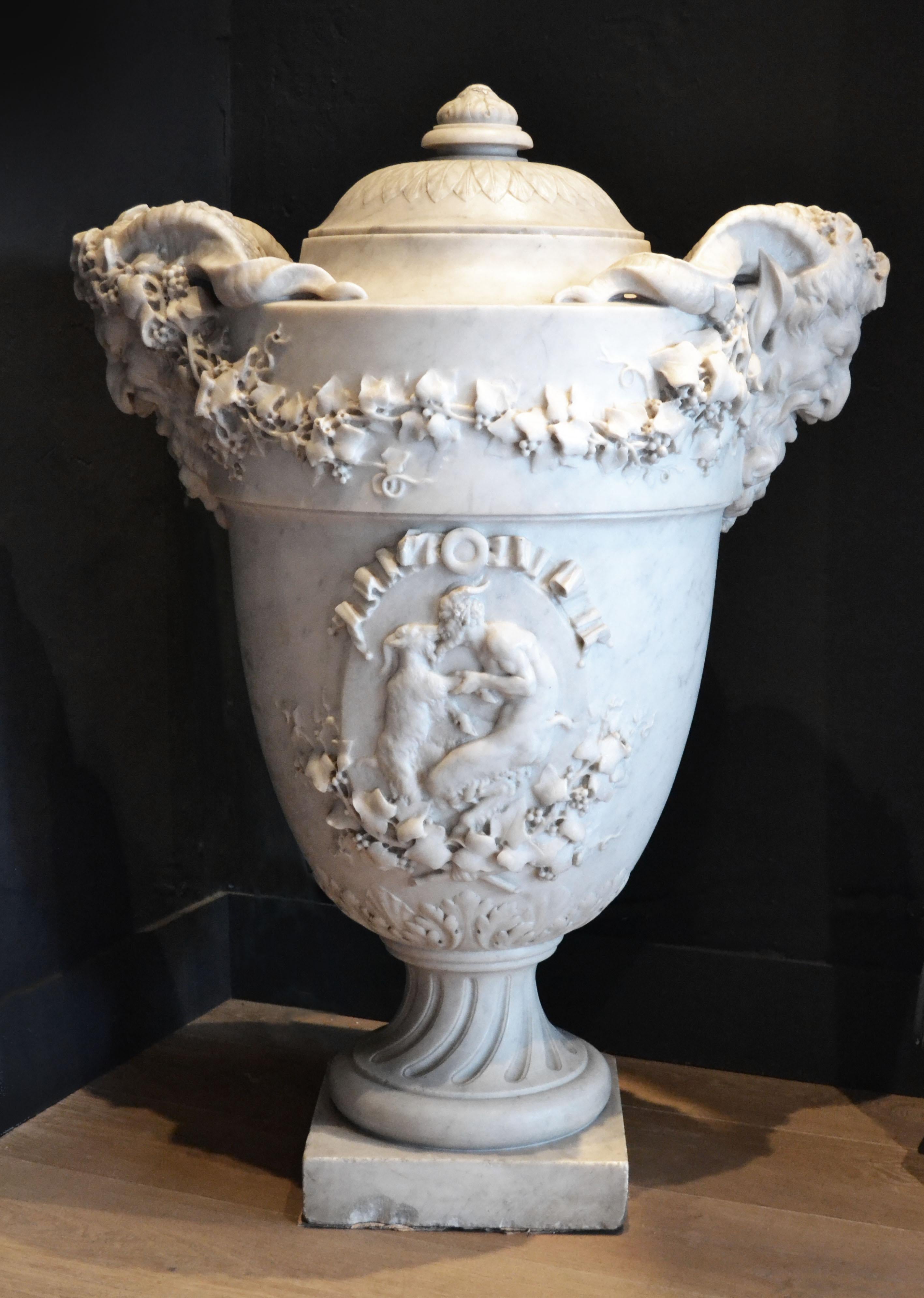 An impressive 19th century Carrara marble lidded company urn. The fine quality carving depicts a dancing faun and the urn is flanked by two satire heads draped with ivy leaf decoration.