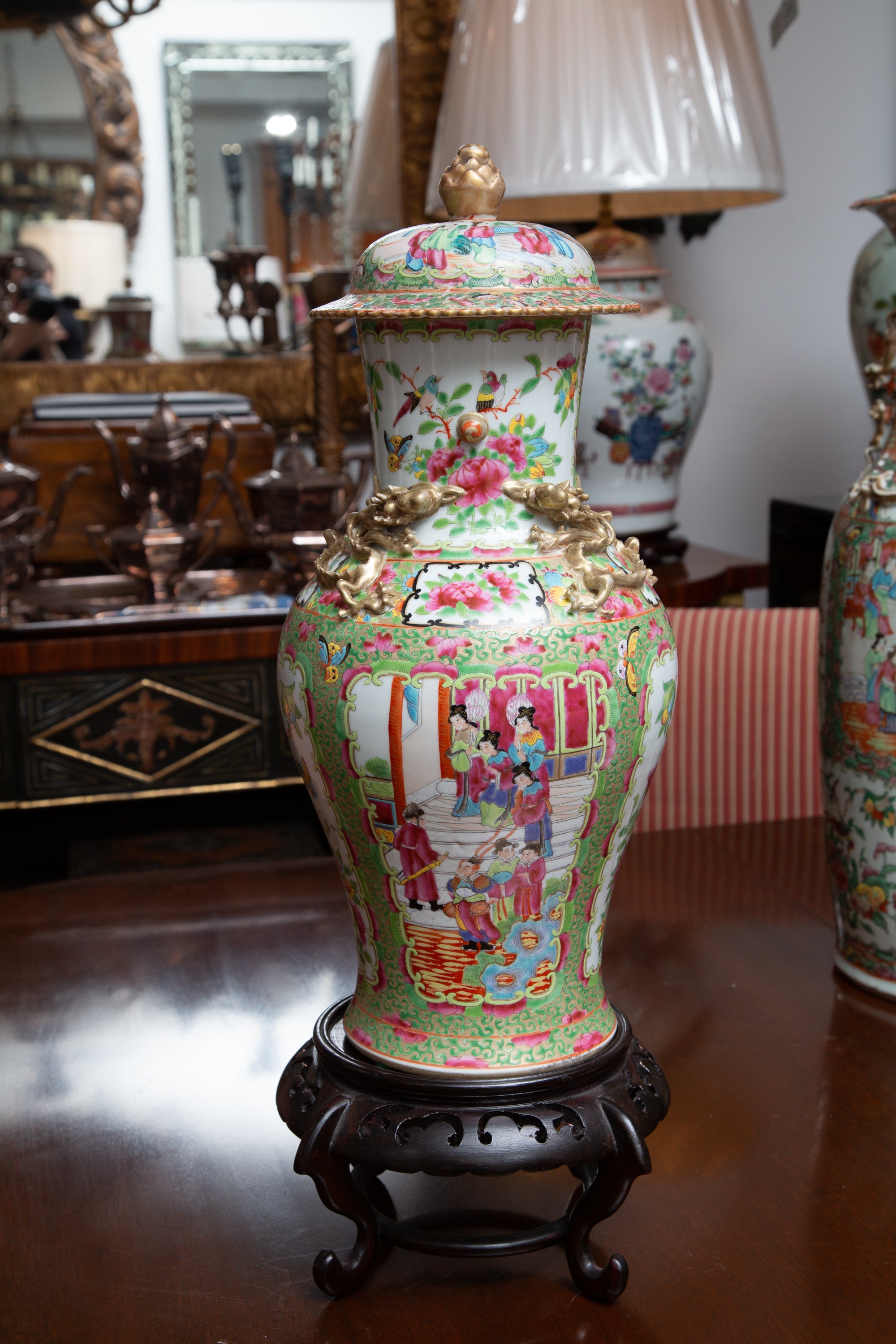 This is an elegant Chinese Rose Medallion lidded vase displaying figures in naturalistic settings, painted in traditional pastel colors and situated on a wooden stand, 19th century.