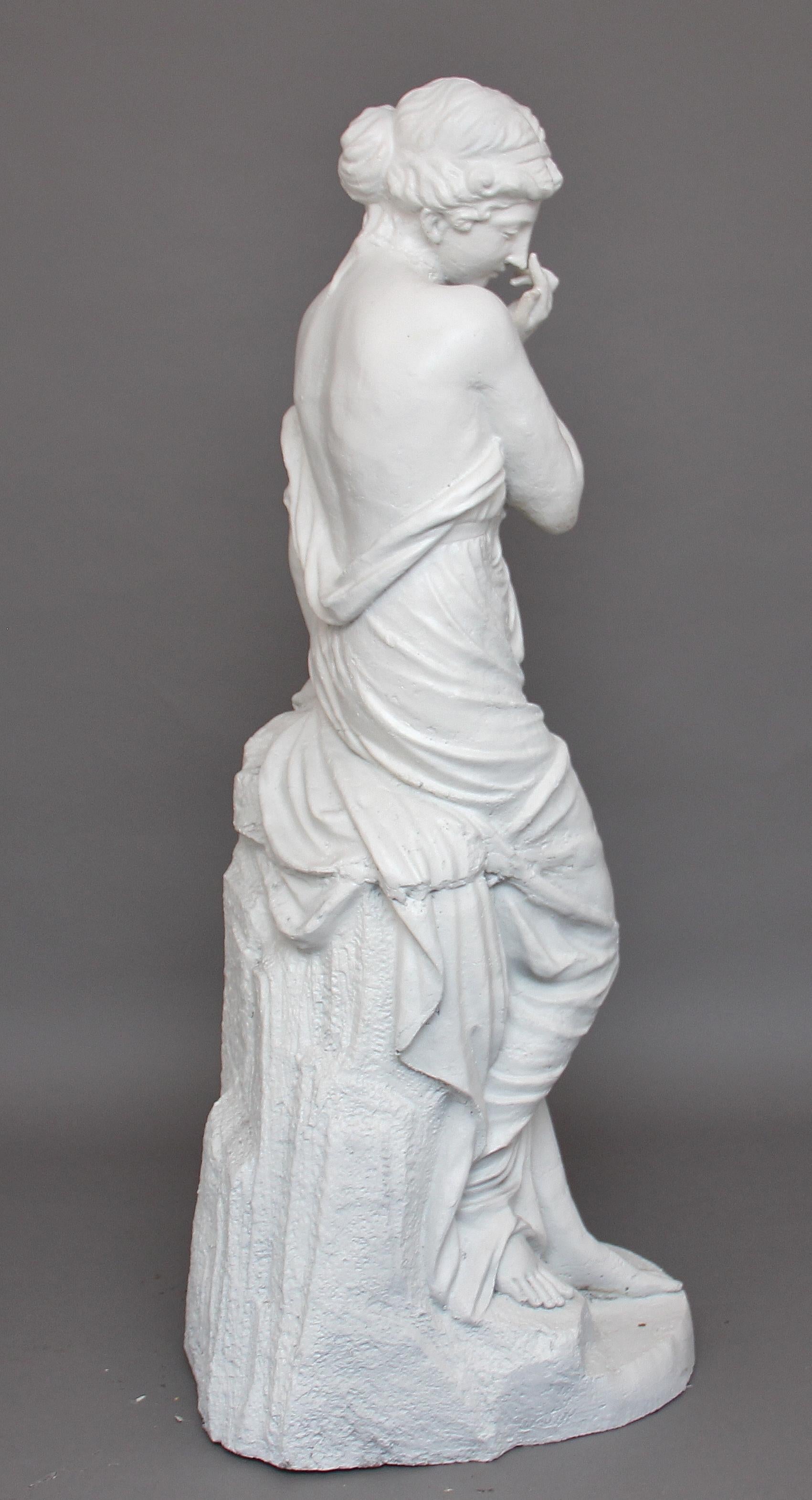A life-size French mid-19th century cast iron statue of a semi clad pretty maiden wearing Classical Greek costume, standing over a broken jug whilst leaning on a wall, circa 1860.
 