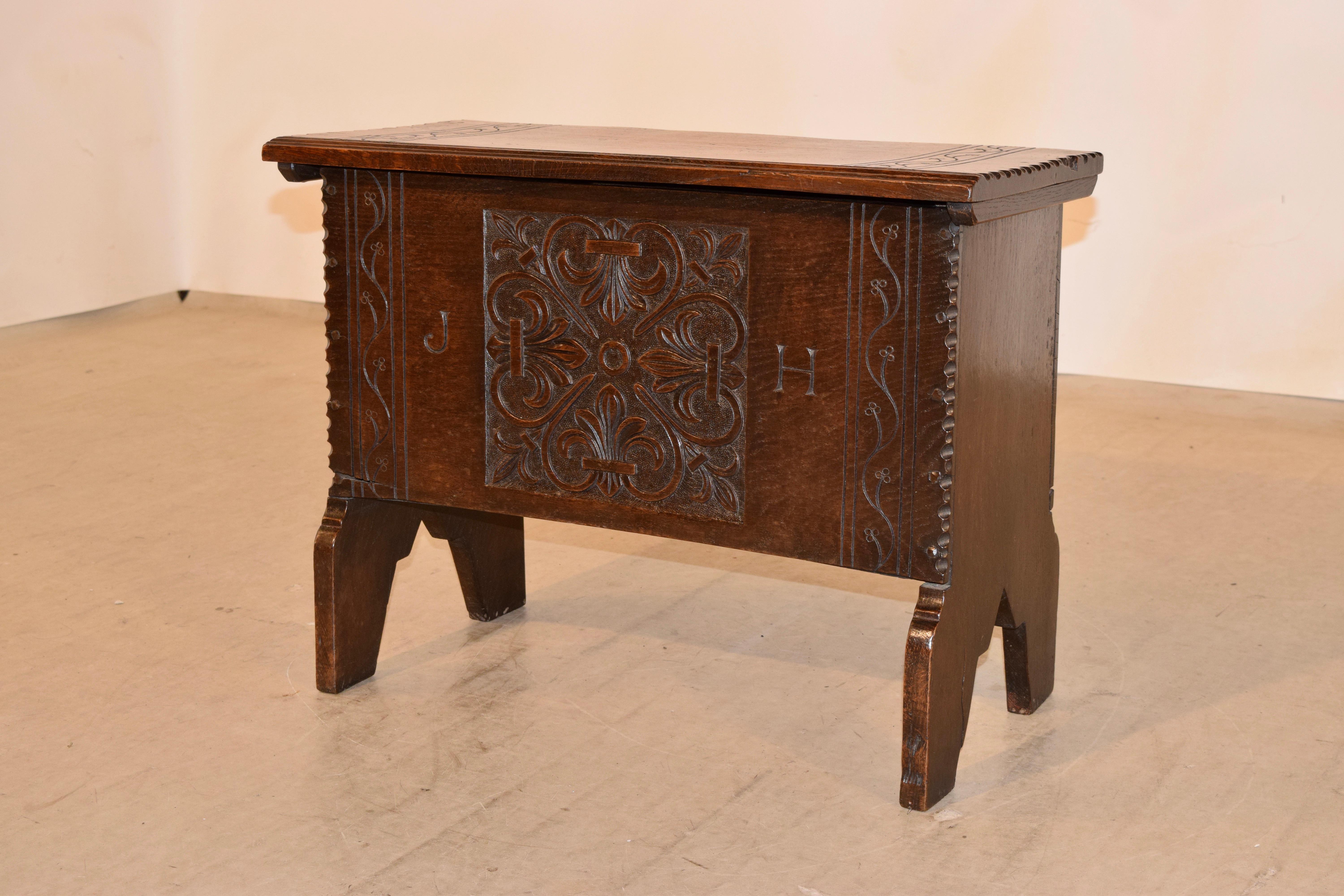 19th century English oak stool with a lift top. The top has hand carved banding, a molded front edge, and pie crust sides. The front has a lovely hand carved decorated central design, flanked by carved banding and the initials J H, along with pie