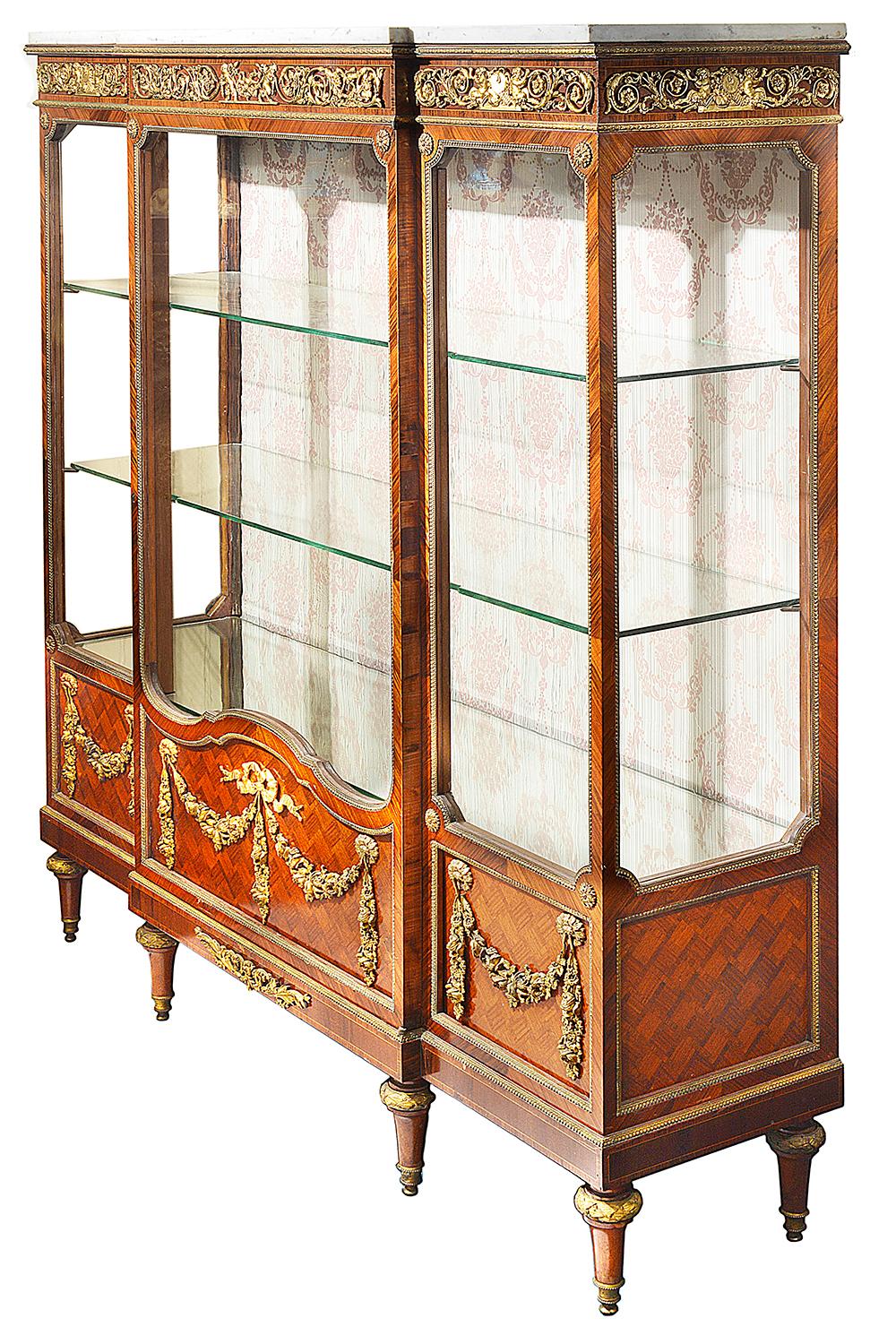 A very good quality late 19th century French parquetry inlaid vitrine / display cabinet.
Having its original Carrera marble top, wonderful gilded ormolu mounts of scrolling foliate decoration with cherubs playing musical instruments, three glazed