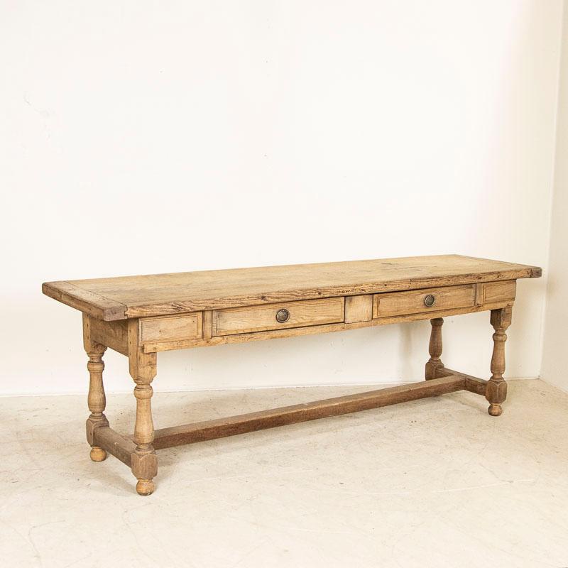 This long refectory or library table is from France. Made of solid oak, the impressive turned legs and long stretcher add to its visual appeal. The raw oak has been bleached, lightening the look which will serve well in today's modern home. The