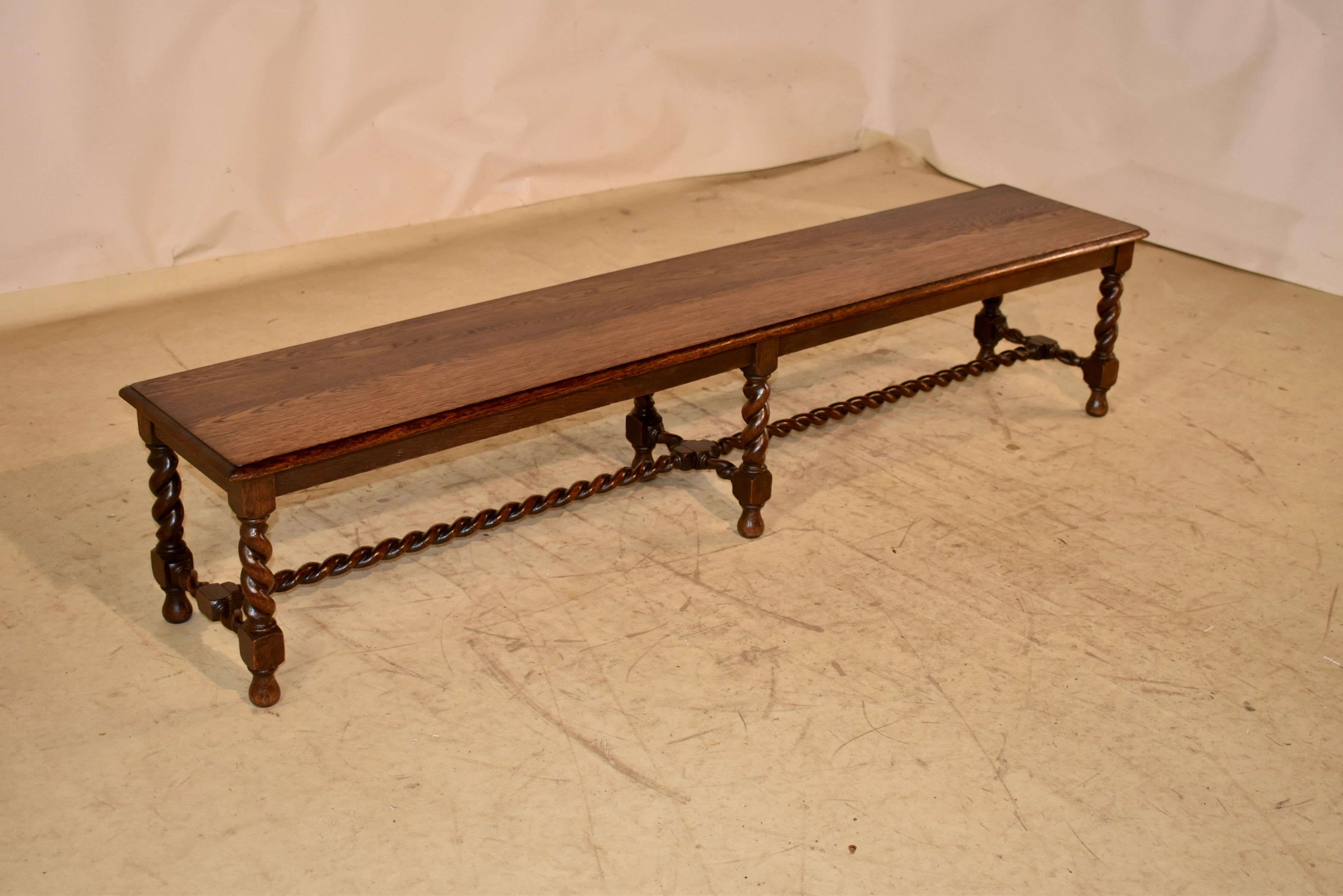 Late 19th century long bench made from oak.  

The top is made from two boards, with a beveled edge surrounding the top.  This follows down to a delightfully simple apron and is supported on hand turned barley twist legs, joined by matching