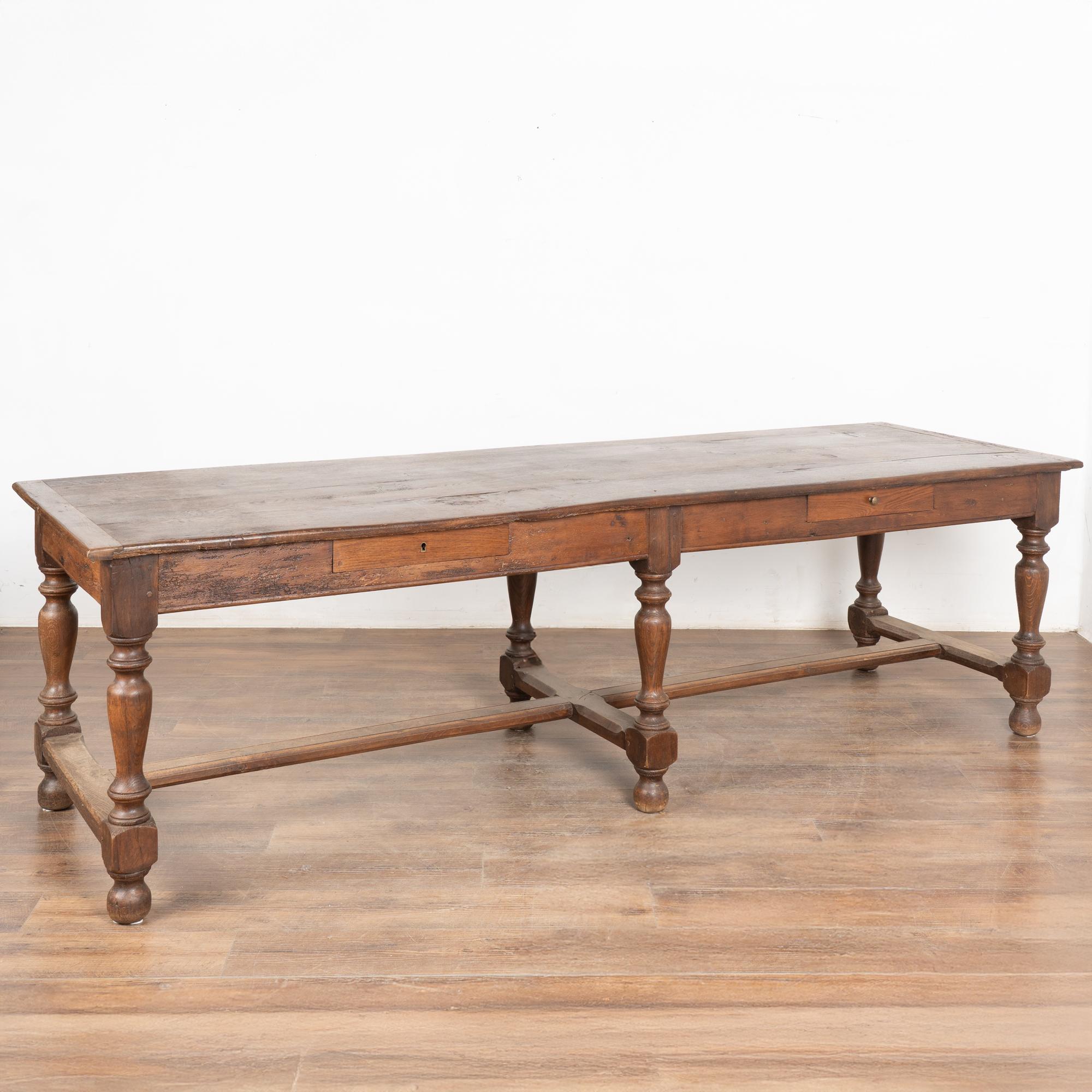The weathered patina of the old oak wood draws one to this long refectory or library table with two functioning drawers from France.
The turned legs of the long stretcher base add to the visual appeal. 
Note in close up photos the wood grain, old