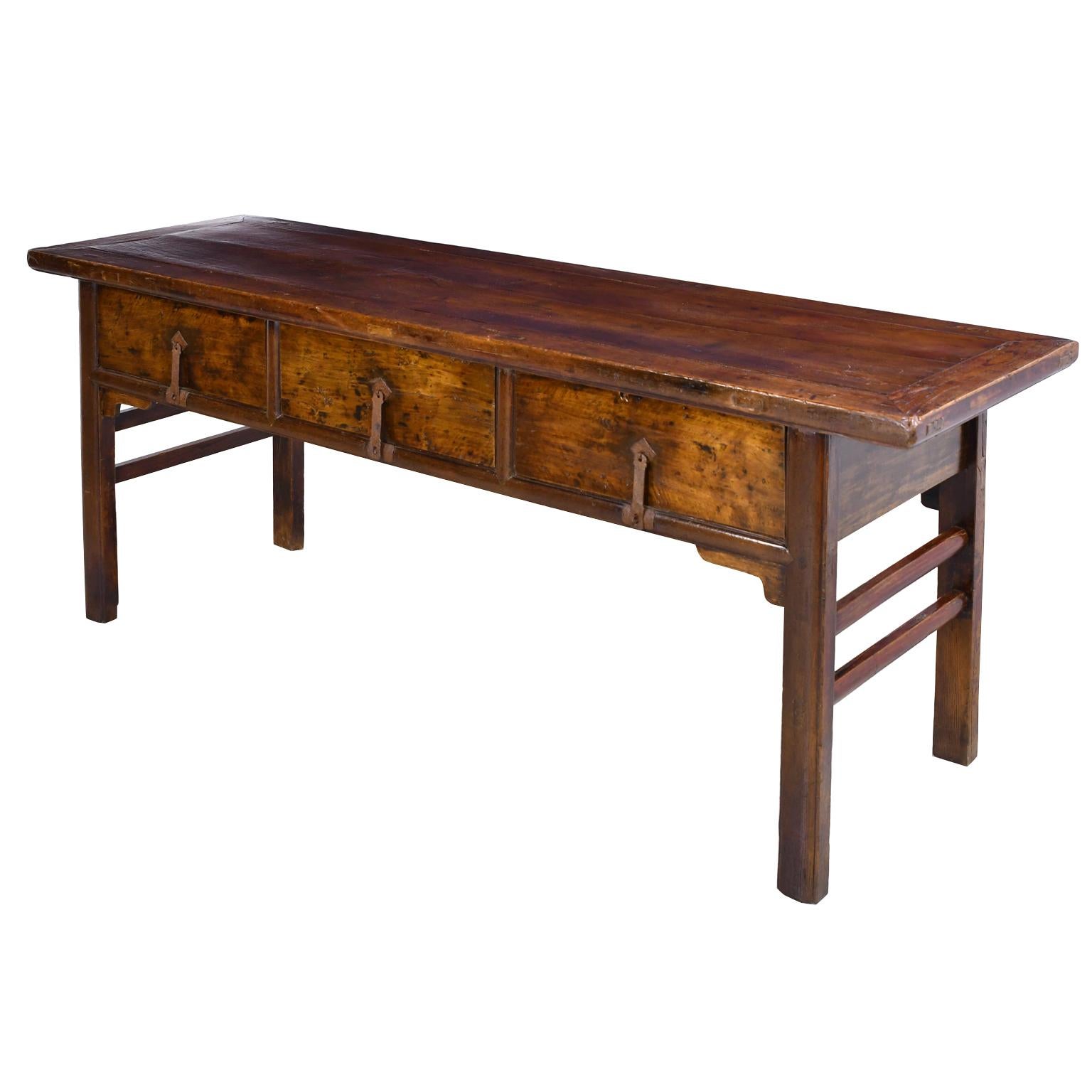 A 19th century Chinese Qing altar table in elm with a thick rectangular top over a base with three drawers that rests on square legs with two side stretchers on each end, and three panels along the length of the back. Drawers have original forged