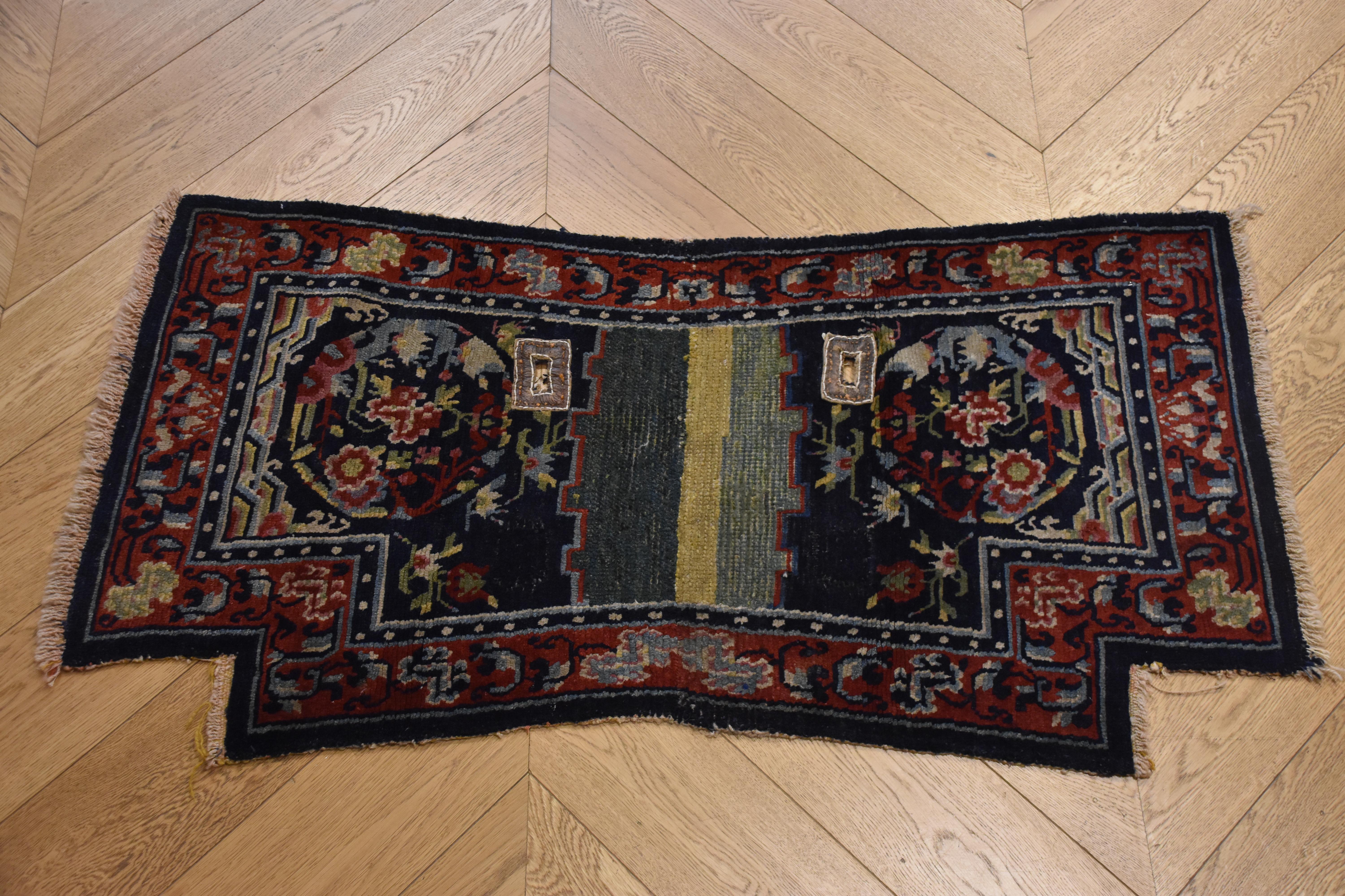 Saddlecloth in Tibetan wool with leather eyelets circa the 1870s. Decorated with floral motifs both in medallions and in rich borders. The peony, which is depicted in the medallions, is a symbol of nobility and refinement. In yin and yang, the peony