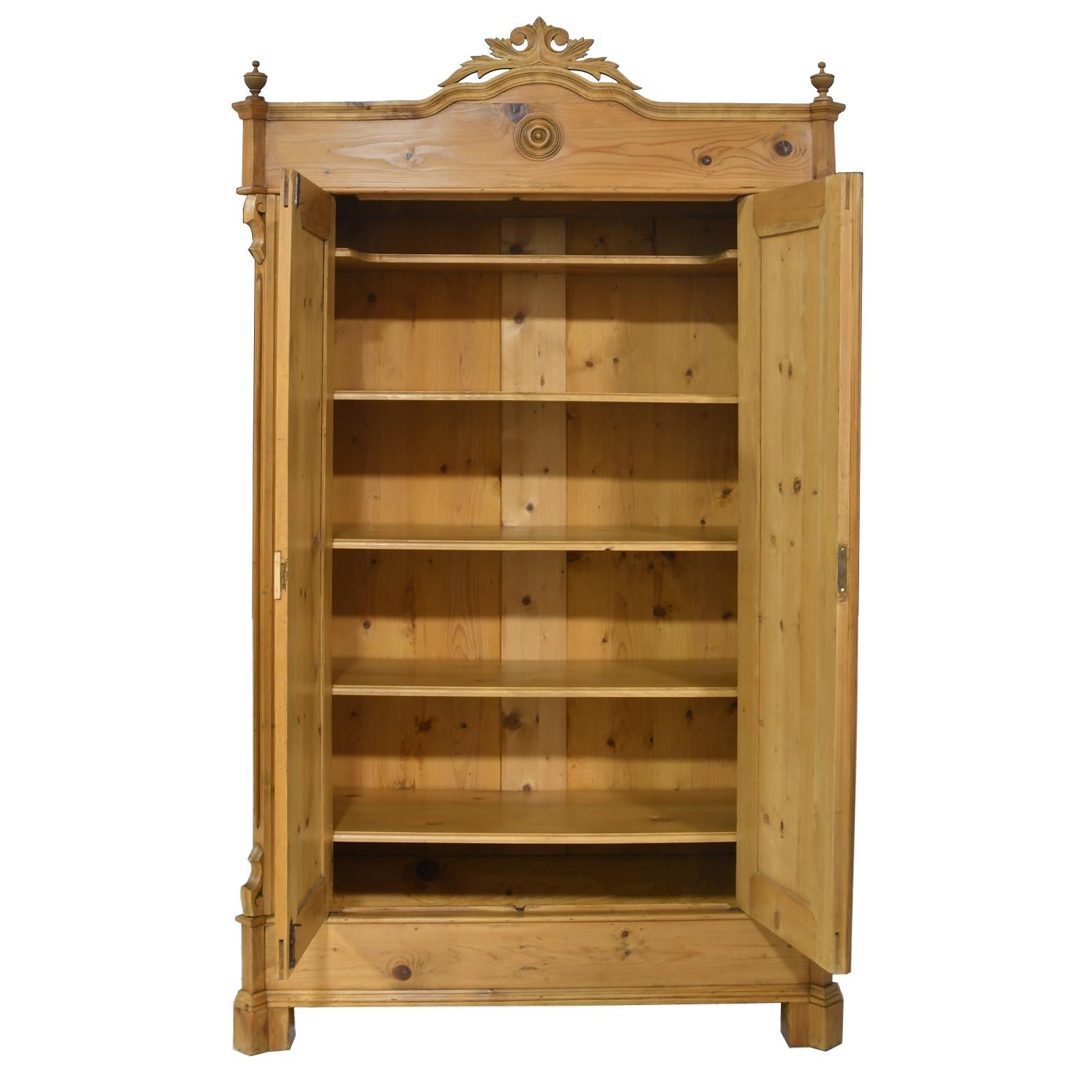 A charming antique Louis Philippe pine armoire with carved foliate bonnet and turned finials on corners of crown molding, with reeded stiles, paneled sides and two paneled doors that open to five adjustable shelves, Germany, circa 1860. Armoire has