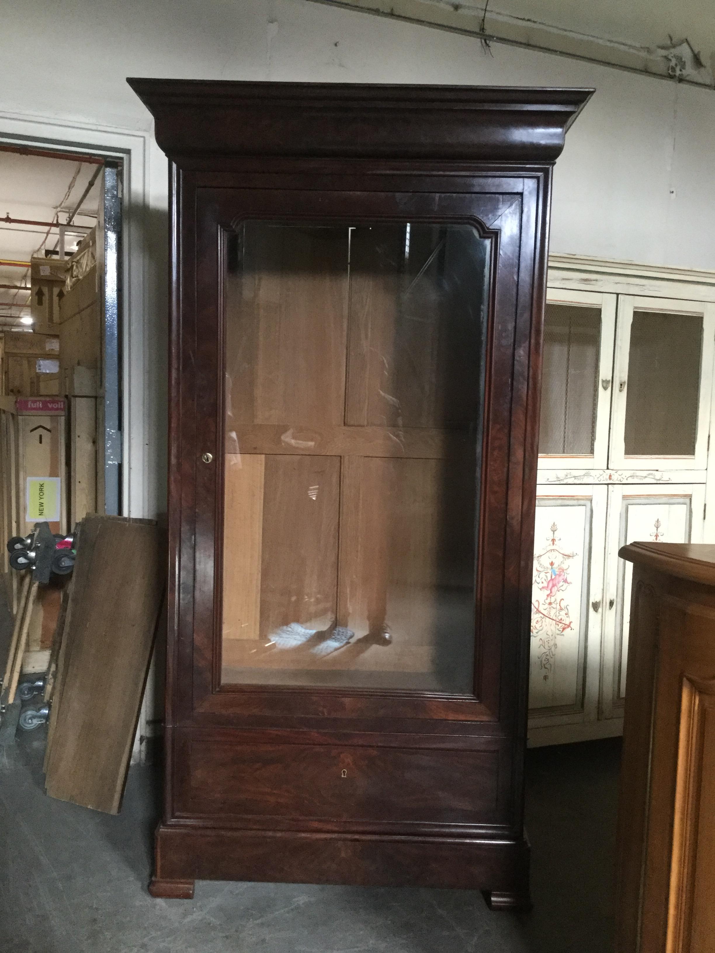 This 19th century Louis-Philippe flame mahogany armoire features a glass door, 3 adjustable shelves and 2 bottom drawers for additional storage. With clean, straight lines, this armoire/bookcase works well in any contemporary interior. Original lock