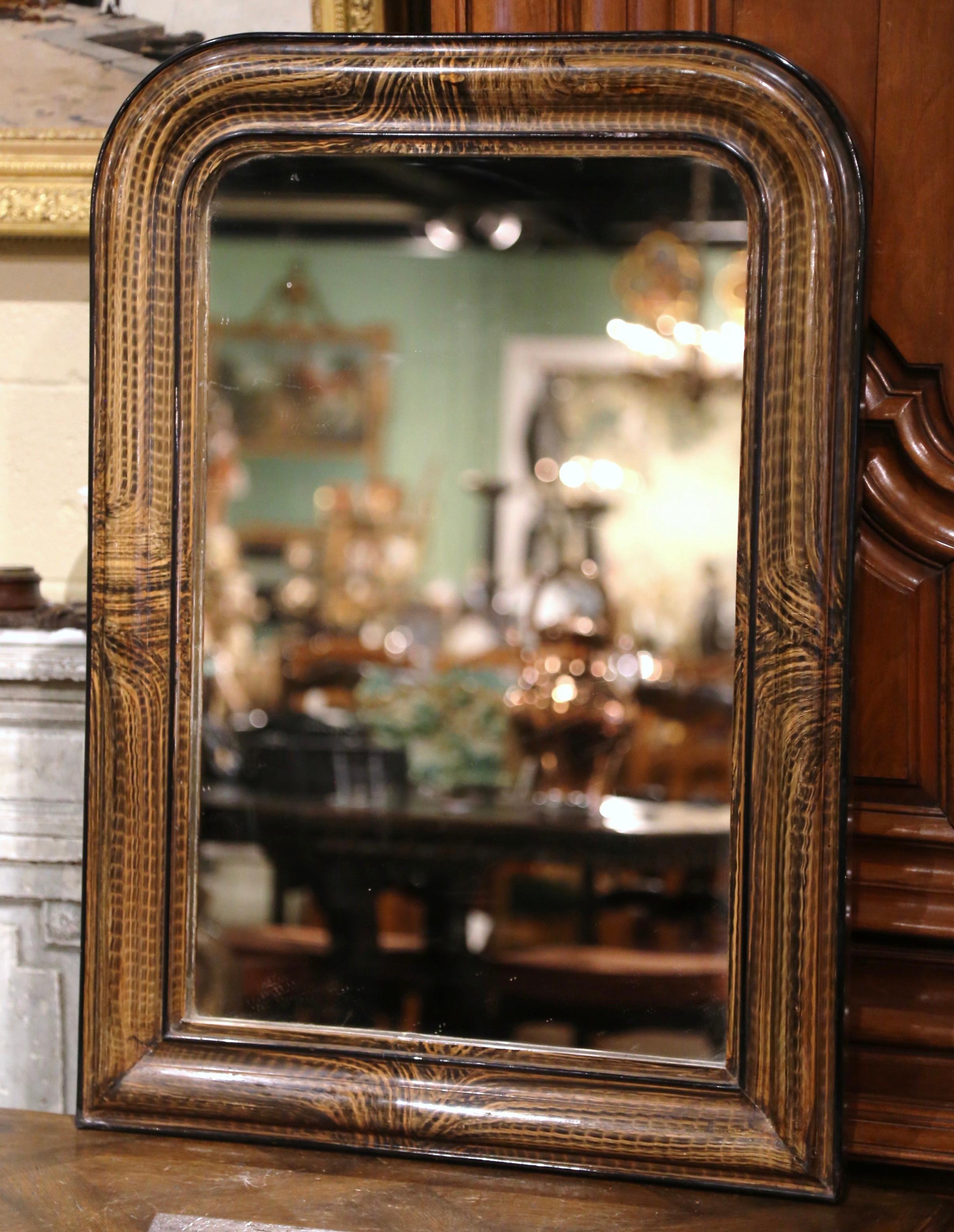 This elegant antique wall mirror was crafted in France, circa 1870. The frame with rounded corners is decorated with faux burl wood motifs in between patinated brown paint finish. The two-tone Louis Philippe style mirror is in excellent condition