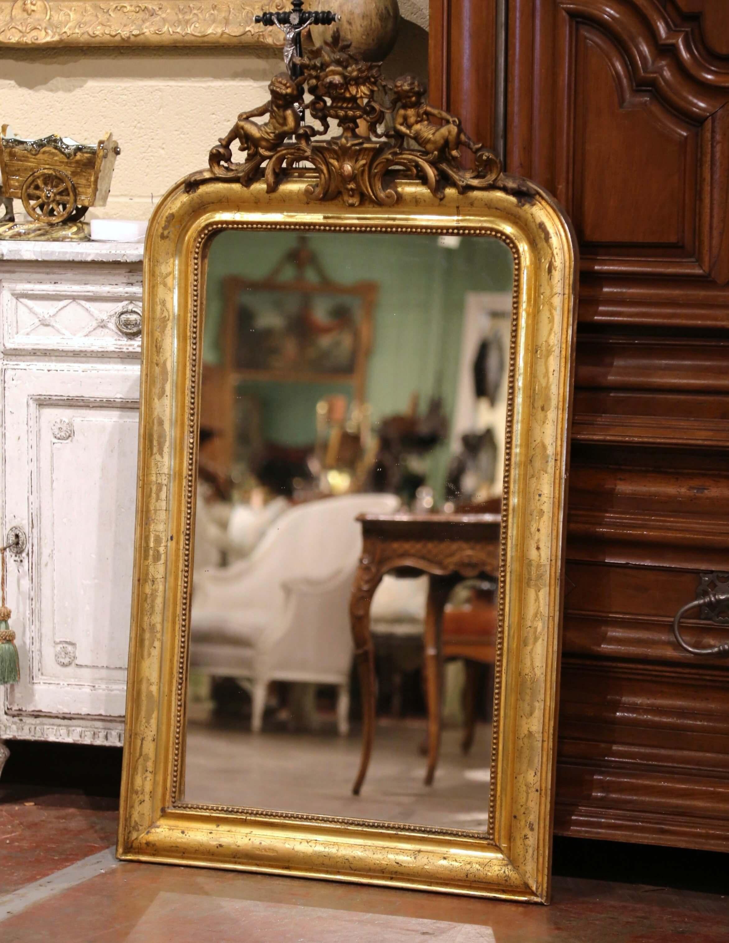 Decorate a powder room with this elegant antique gilt mirror! Crafted in France, circa 1870, the mirror is decorated at the pediment with a flower vase cartouche in the center flanked by a pair of carved cherub figures. The gilt frame, dressed with