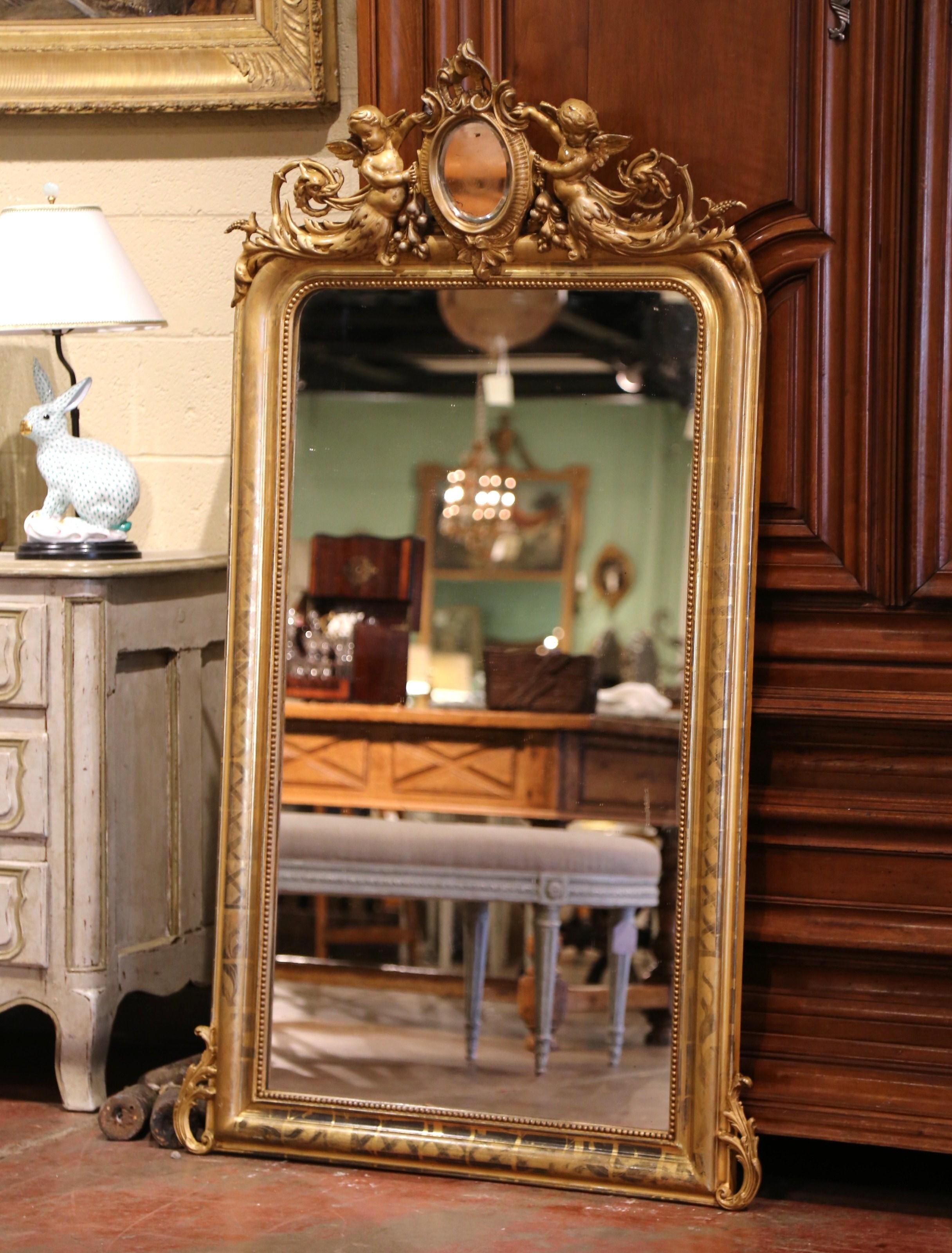 This elegant, antique wall mirror was crafted in Paris, France, circa 1870. The mirror is decorated at the pediment with a small oval cartouche mirror in the center held by a pair of carved cherubs. The gilt frame, dressed with the original mercury