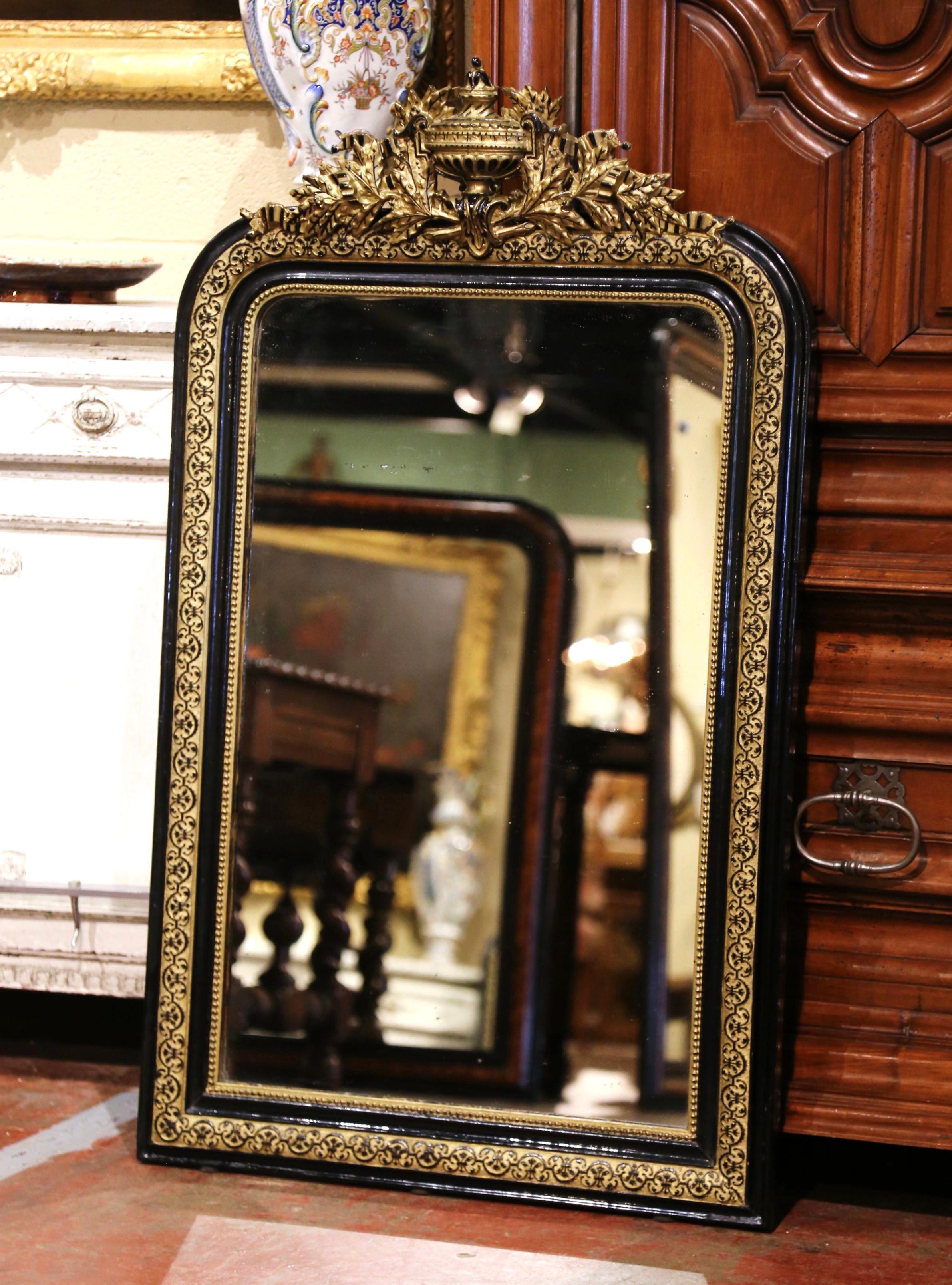 This elegant, antique wall mirror was crafted in France, circa 1880. The mirror is decorated at the pediment with a large cartouche vase in the center flanked with carved floral and leaf motifs on both sides. The two-tone gilt and blackened frame,