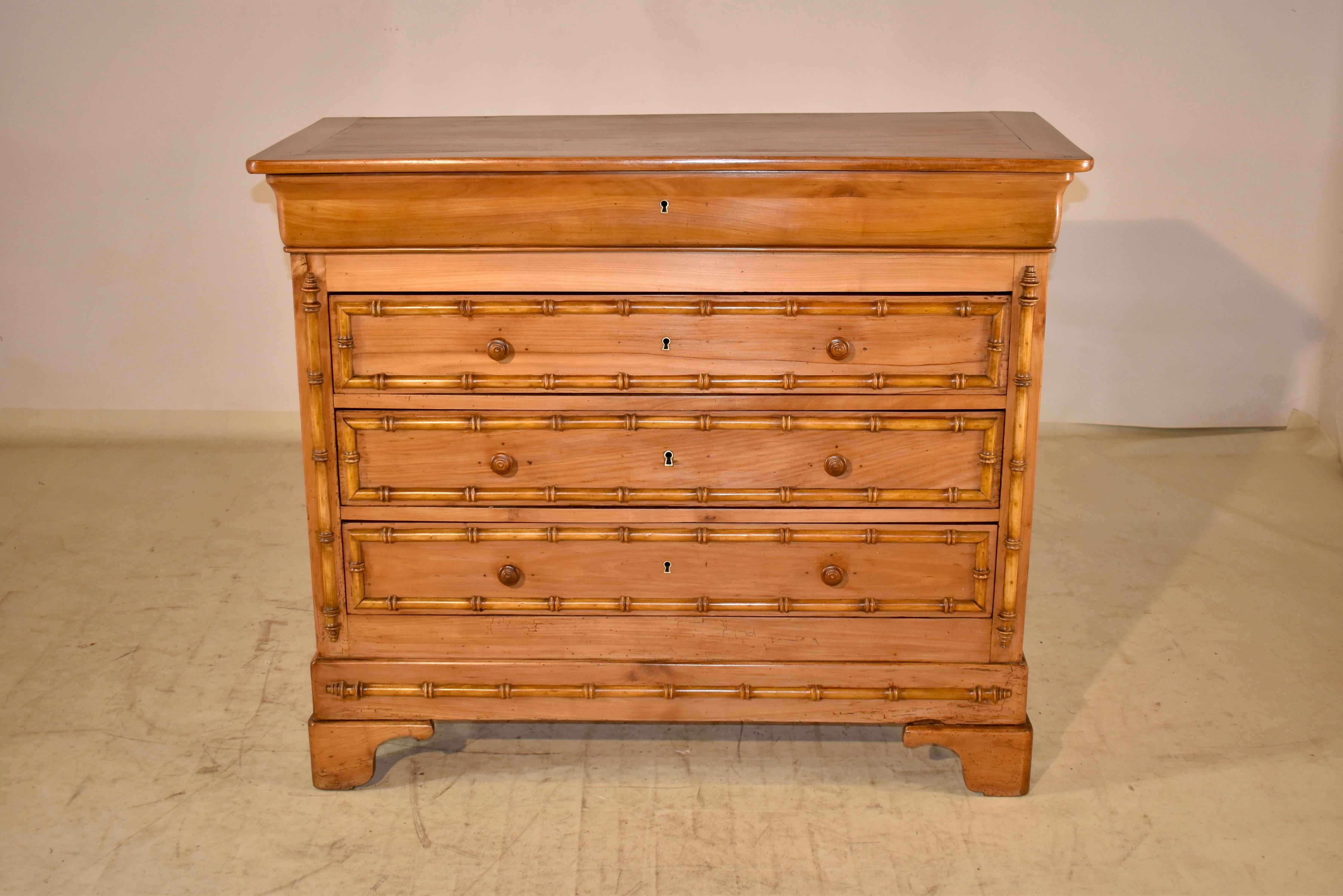 19th century cherry commode from France. The top is banded and is wonderfully figured. The sides are simple and paneled, and the front of the case has a molded apron, which is a hidden drawer, over three drawers, all with faux bamboo molded accents.