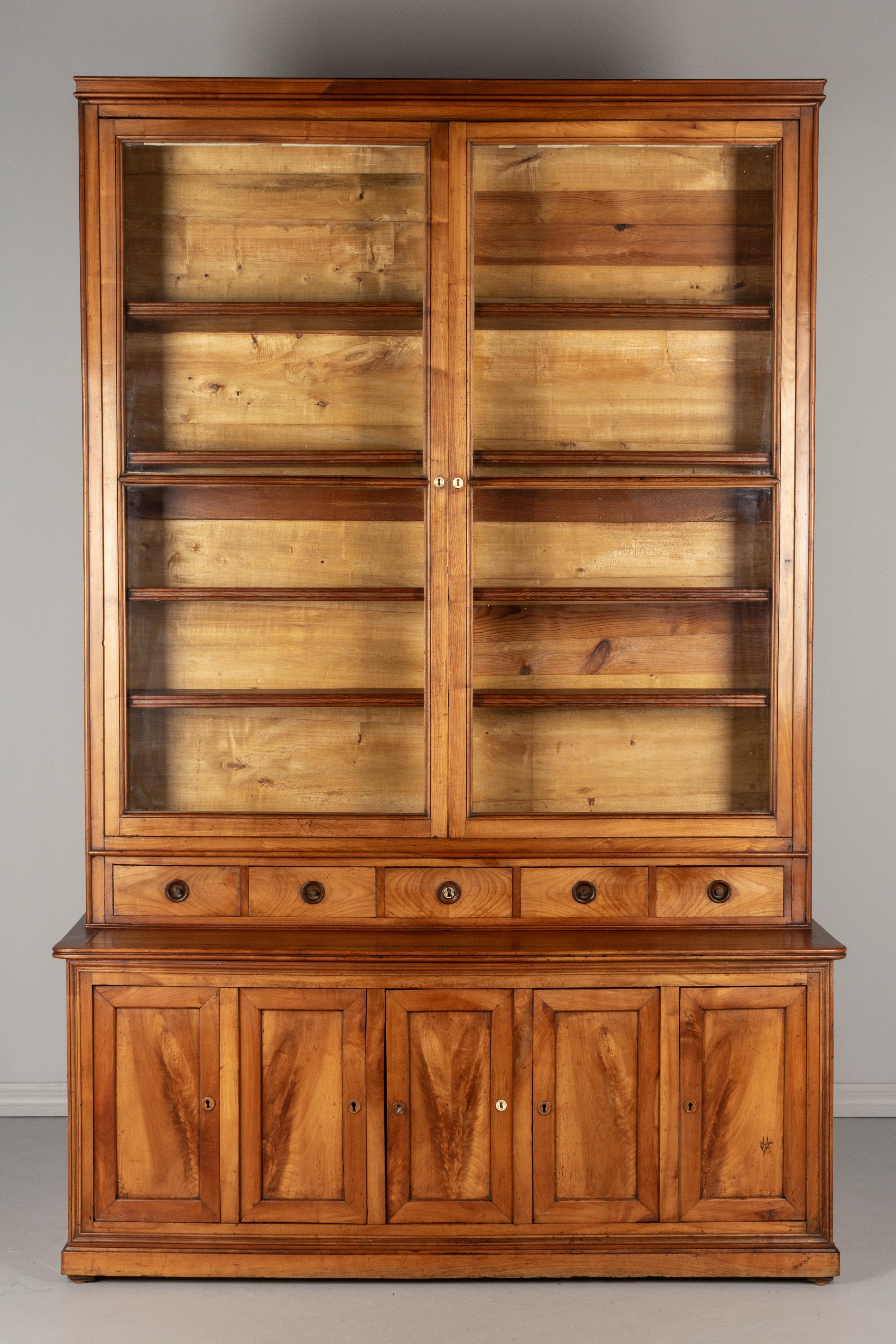 A 19th century French Louis Philippe, bibliotheque or display cabinet, made of solid cherrywood. This cabinet was purchased in the North of France and was used for display in a retail shop. The upper part has the original glass paned doors with the