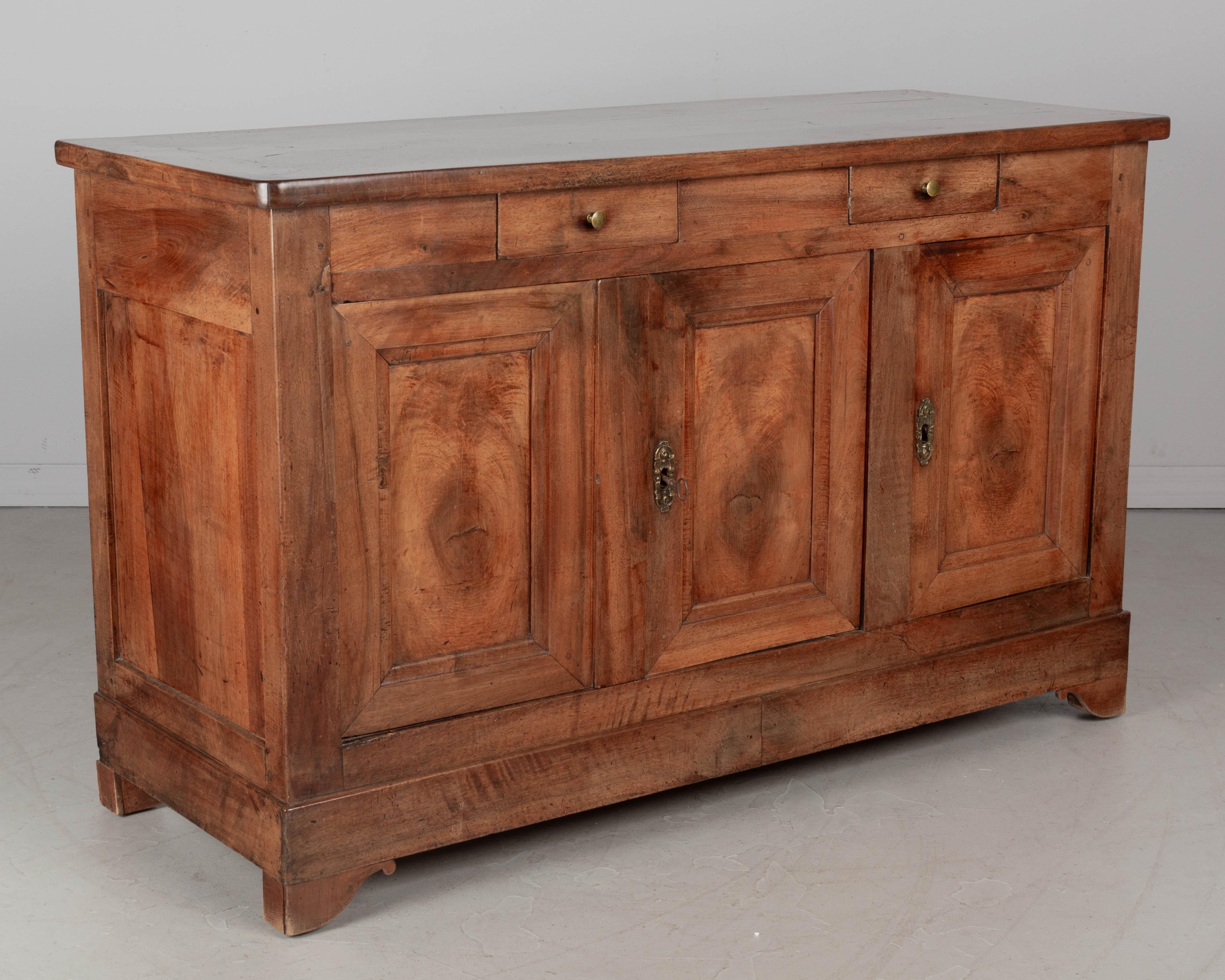 An early 19th Century French Louis Philippe enfilade, or sideboard made of solid walnut. Three paneled doors made from thick planks of walnut, each framing a large knot in the wood grain. Two dovetailed drawers for silverware. Original cast brass