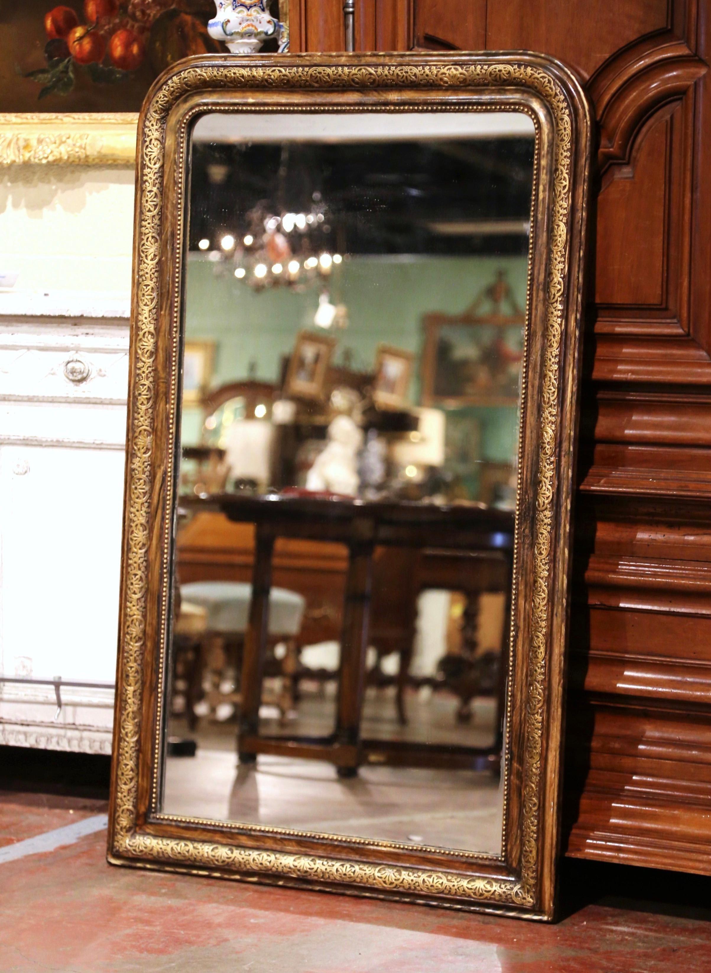 This elegant antique wall mirror was crafted in France, circa 1870. The large frame is decorated with delicate repousse geometric and foliage motifs, further embellished with bead decor around the mirror. The two-tone brown and gilt piece is in