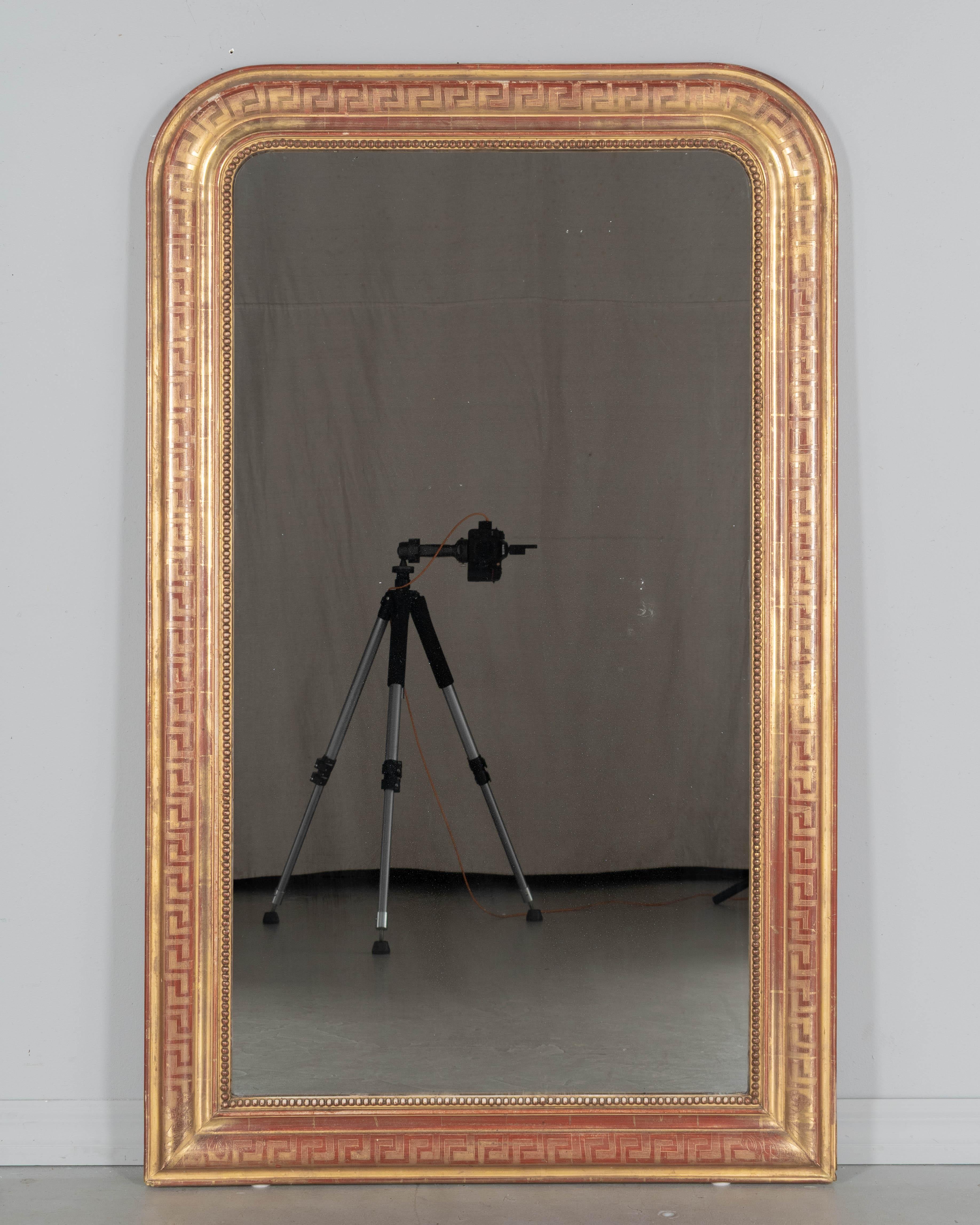 Espejo francés de madera dorada de finales del siglo XIX, estilo Louis Philippe, con diseño de llave griega grabada, esquinas superiores curvadas y borde interior de cuentas. Bonita pátina con roce rojo y acabado dorado cálido. Pequeñas pérdidas de