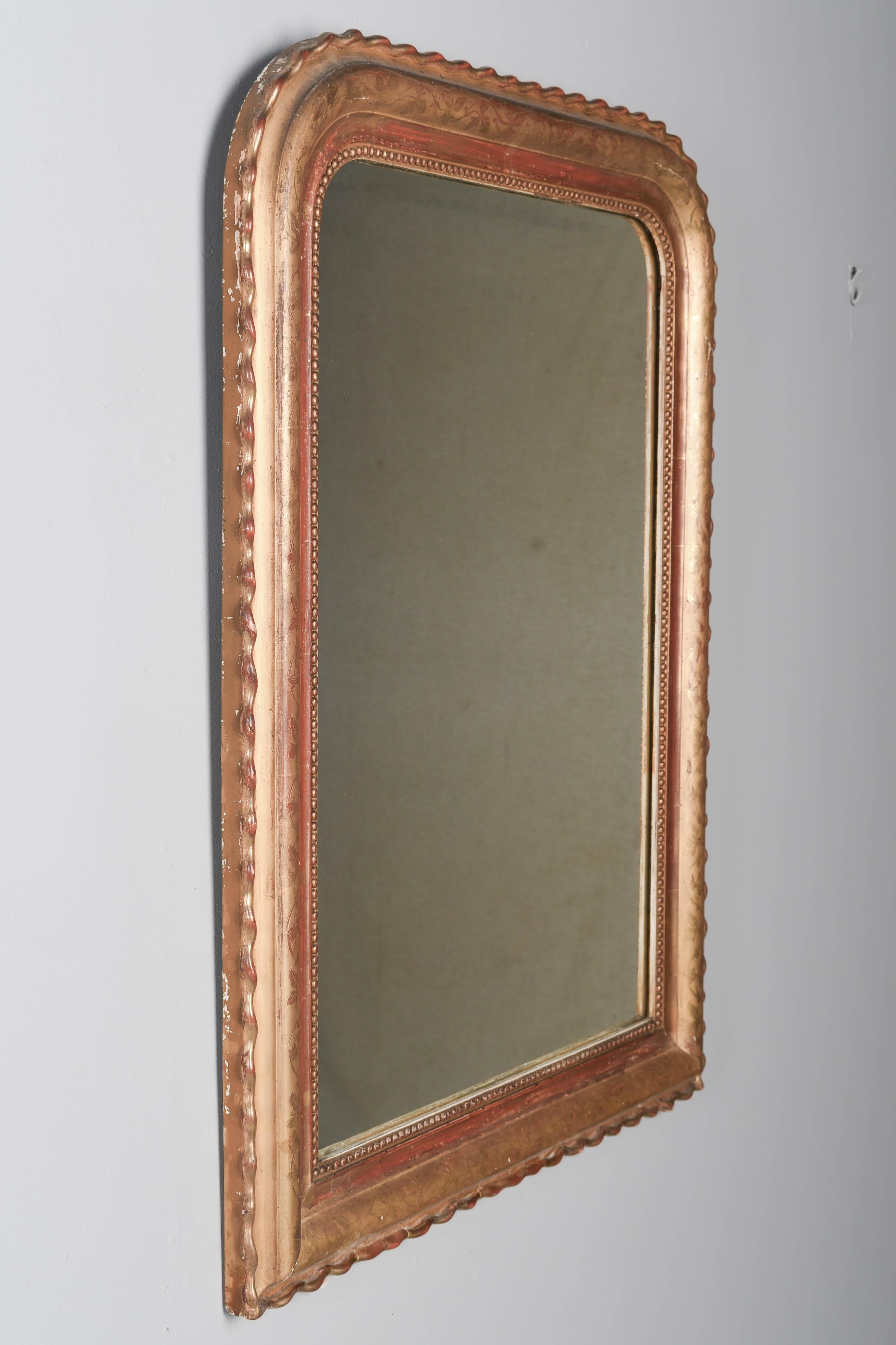 Specchio dorato Louis Philippe del XIX secolo con angoli superiori curvi, bordo esterno ondulato, decorazione a vite incisa e bordo interno a perline. Finitura dorata calda con argilla rossa a vista sotto lo sfregamento. Buone condizioni con piccole