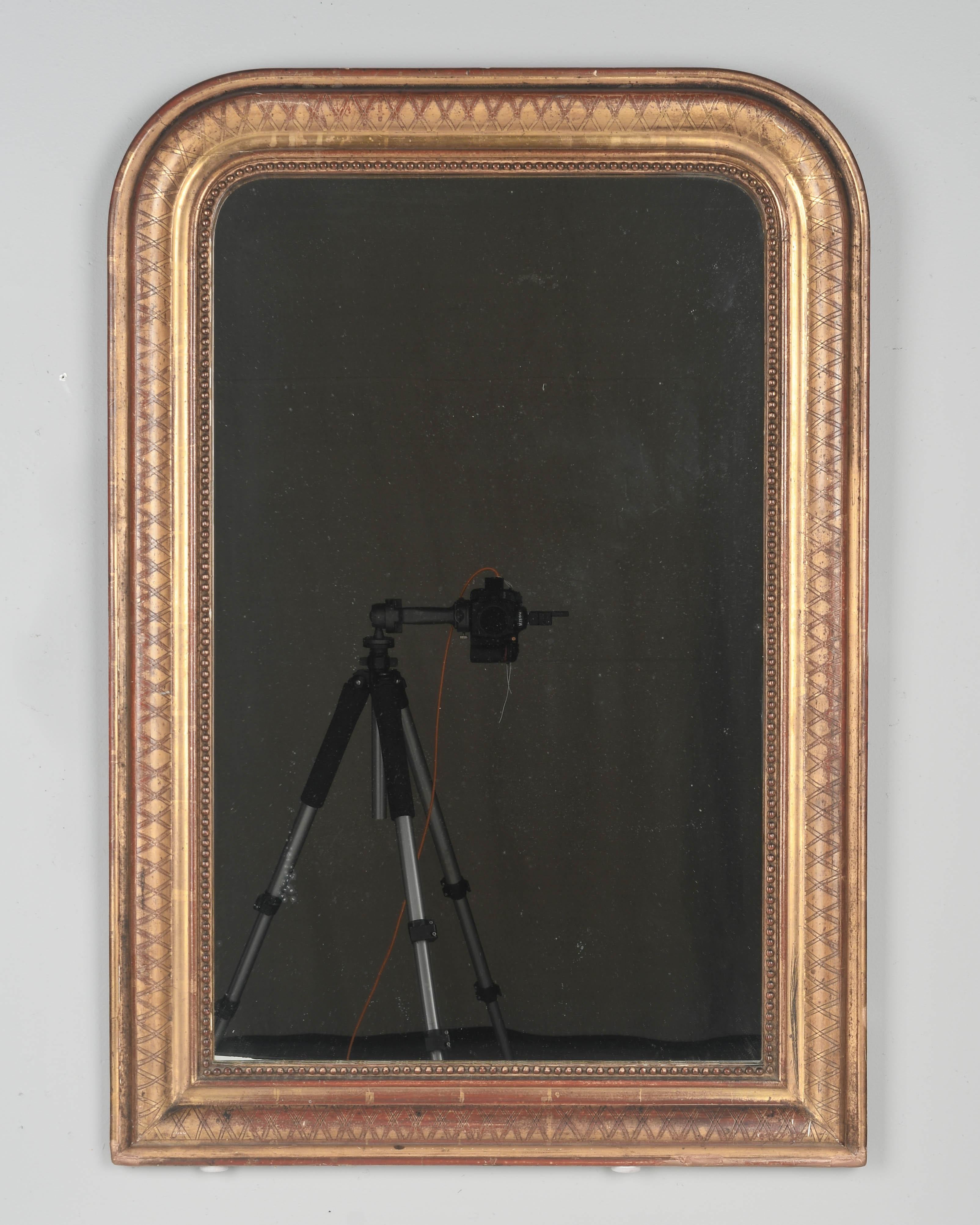 A 19th century French Louis Philippe gilded mirror with curved top corners,  incised x pattern and inner bead border. Warm gilt finish with exposed red clay under rub. Good condition with minor losses and touch ups to gilt. Original mirror. Please