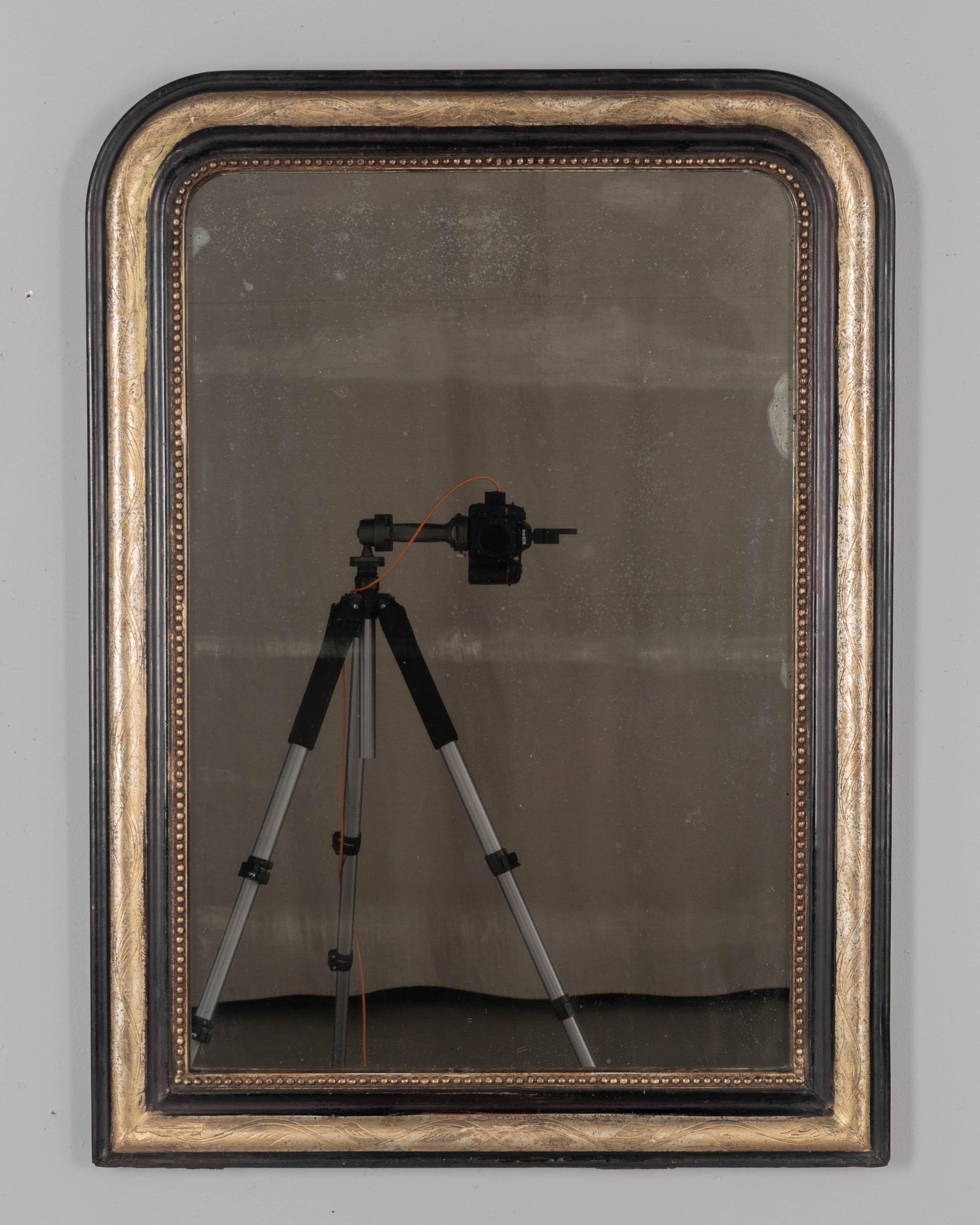 Miroir français Louis Philippe/Napoléon III du XIXe siècle, avec des angles supérieurs incurvés, un motif incisé de feuilles de vigne dorées et une bordure intérieure en perles. La finition peinte en noir et dorée est en bon état, avec quelques