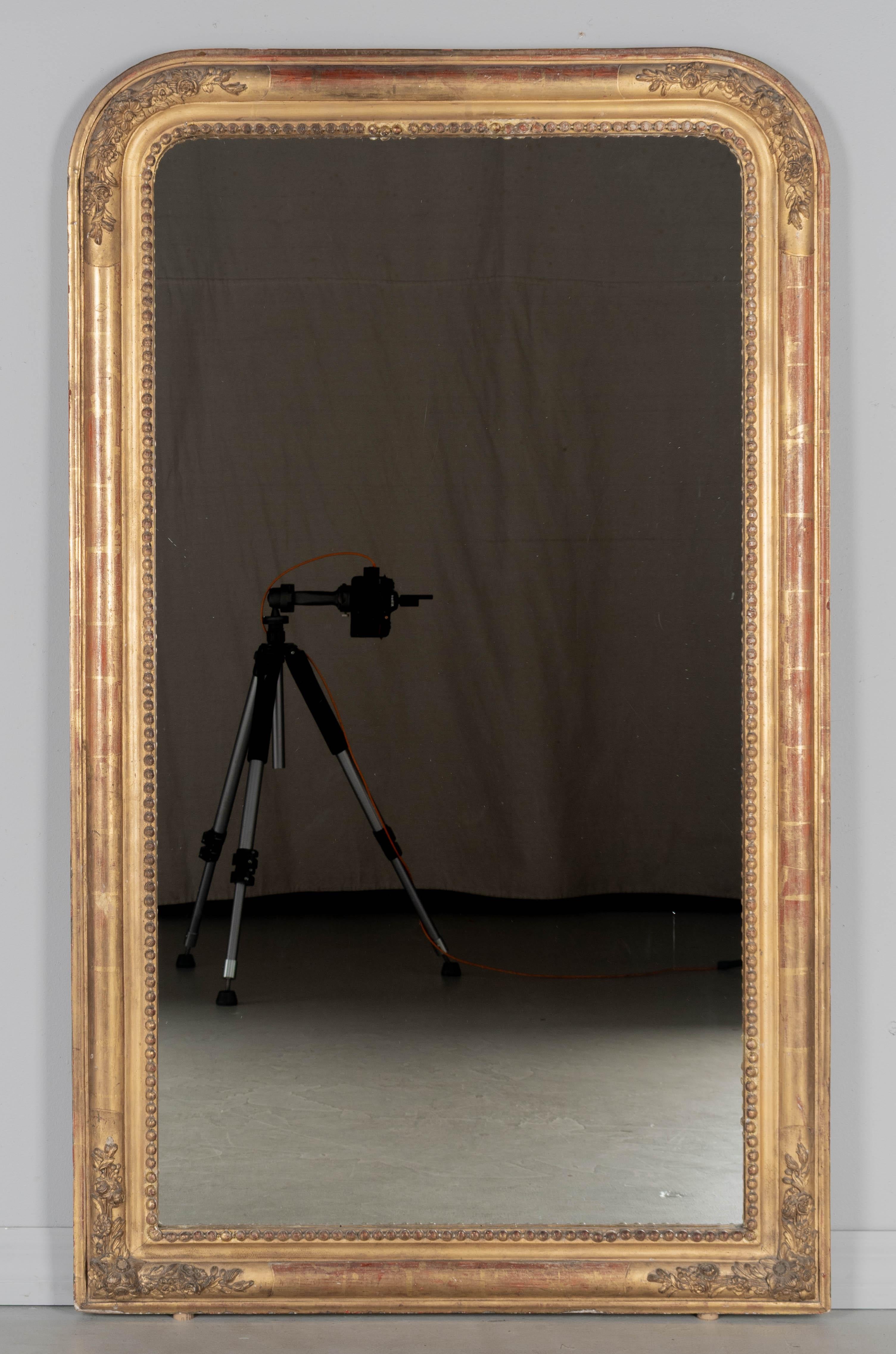 A late 19th century French Louis Philippe style giltwood mirror with floral corner decoration, curved top corners and inner bead border. Nice patina with red under rub and worm gilt finish. Several beads have been replaced and there is some touch