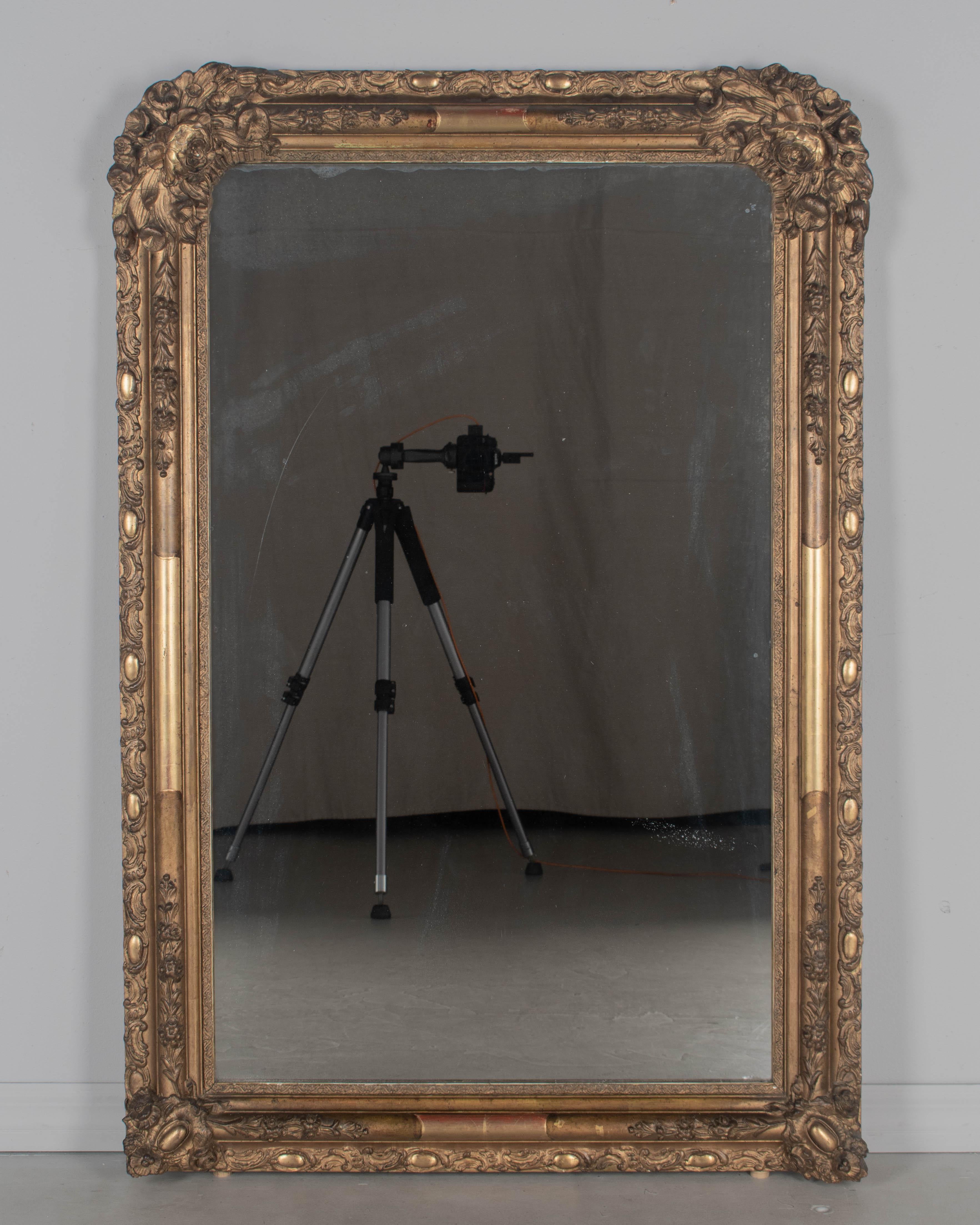 A mid 19th century French Louis Philippe style giltwood mirror with floral decoration. Elaborately detailed with large rosebuds in the upper curved corners. Warm gilt finish with some exposed red under rub and dark patina. In good condition with
