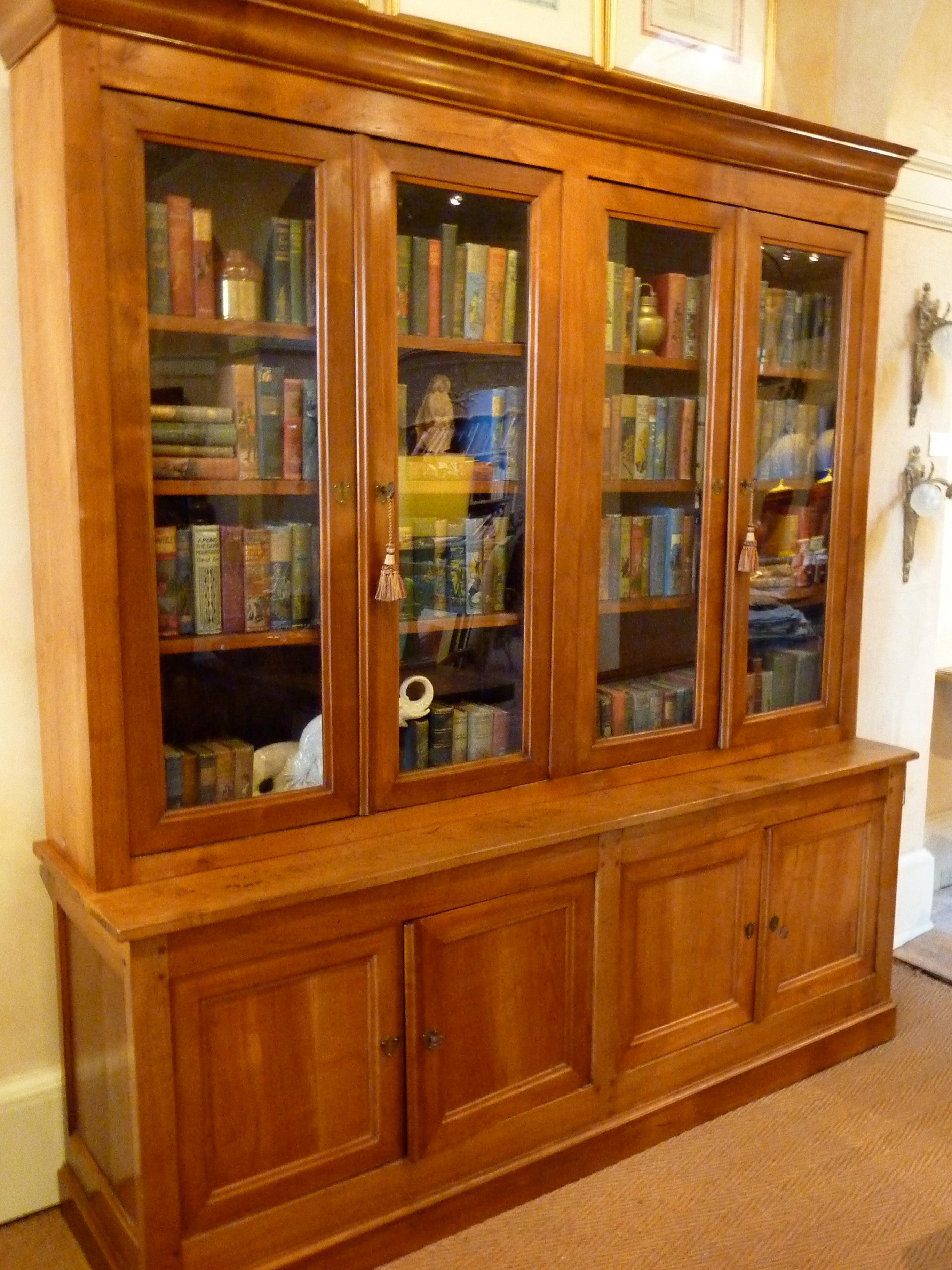19th century Louis Philippe French Provincial “Bibliotheque” (Bookcase). Elegant proportions made of richly patinated cherrywood. The upper bookcase with a shaped cornice above four long molded and glazed doors. The lower buffet with four molded
