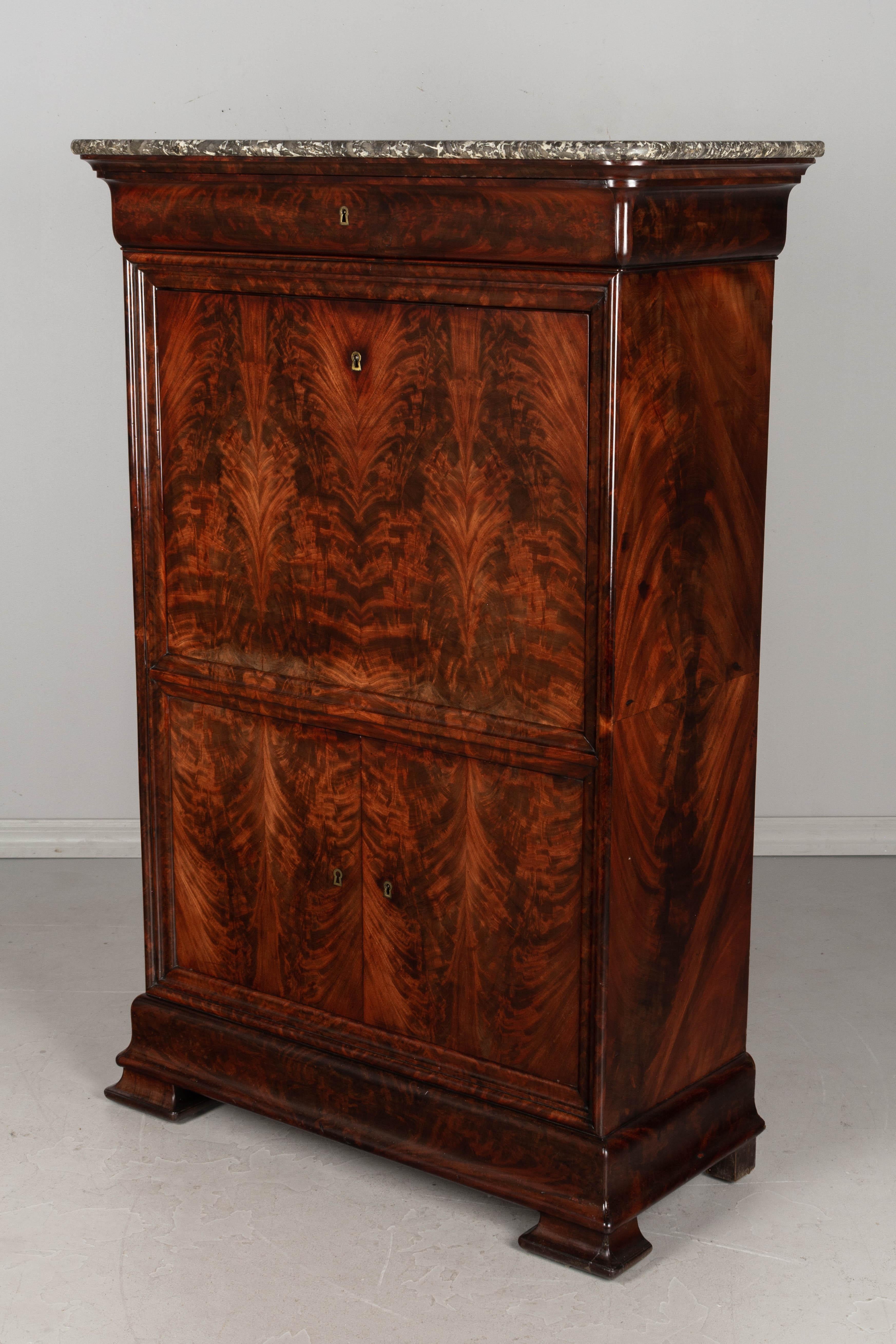 An exquisite early 19th century Louis Philippe French secretaire à abattant, or fall front secretary, made of solid mahogany with beautifully patterned flame mahogany veneer and original grey veined marble top. The main body contains one upper